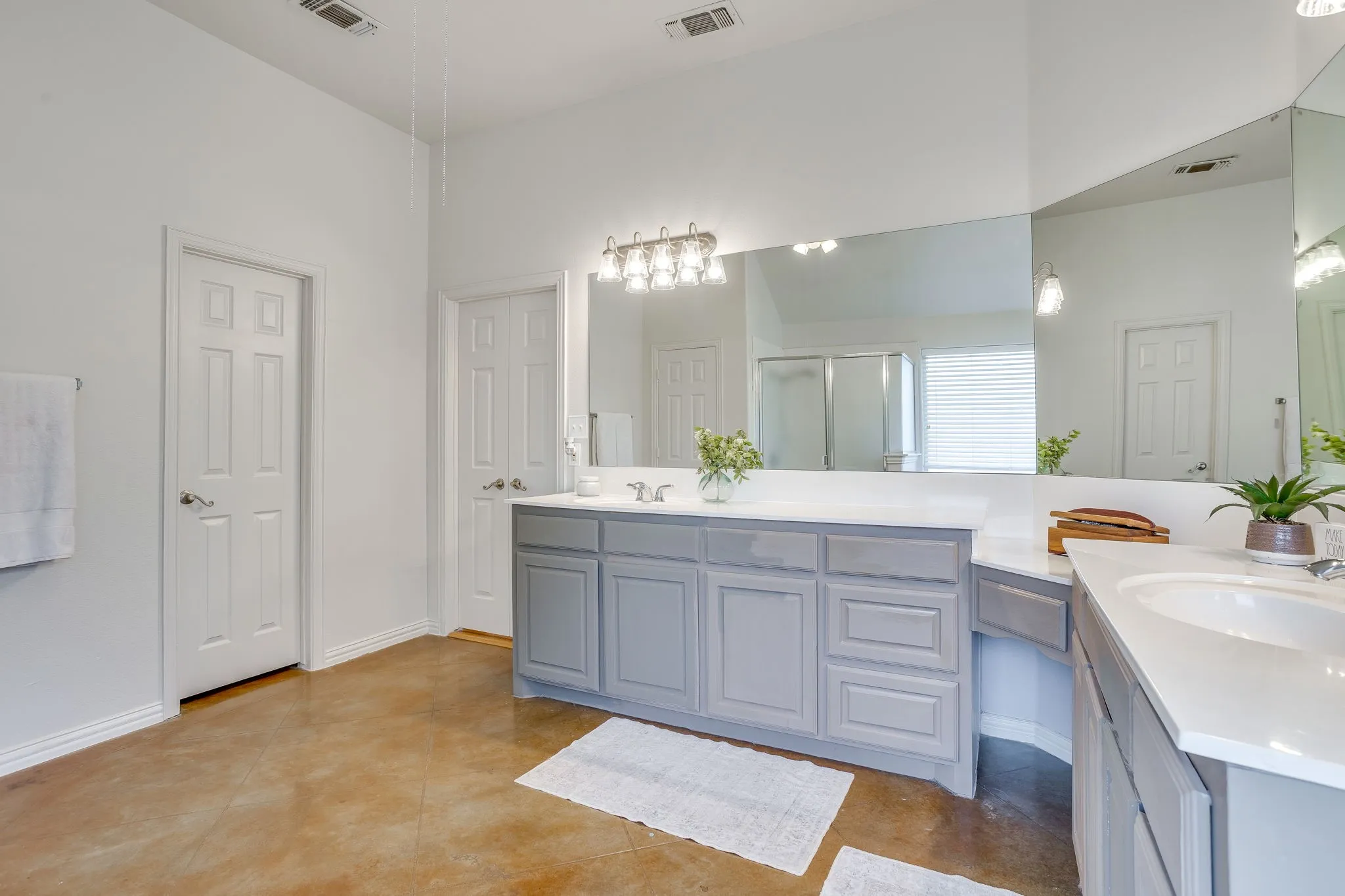 Expansive vanity with light gray cabinetry, white countertops, dual integrated sinks, and an oversized wall-mounted mirror