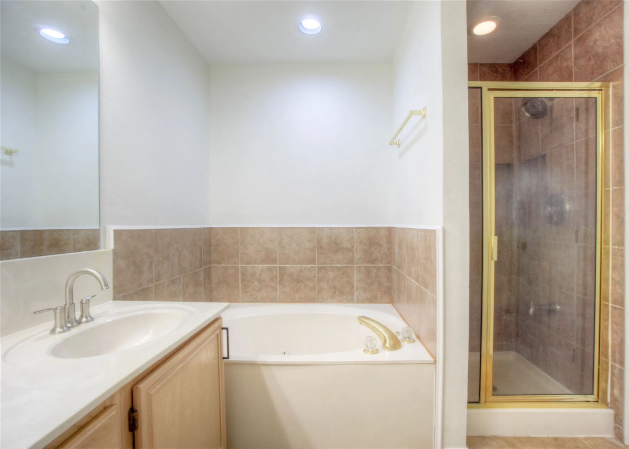 Vanity with integrated sink, built-in bathtub, and enclosed shower with a gold-tone frame