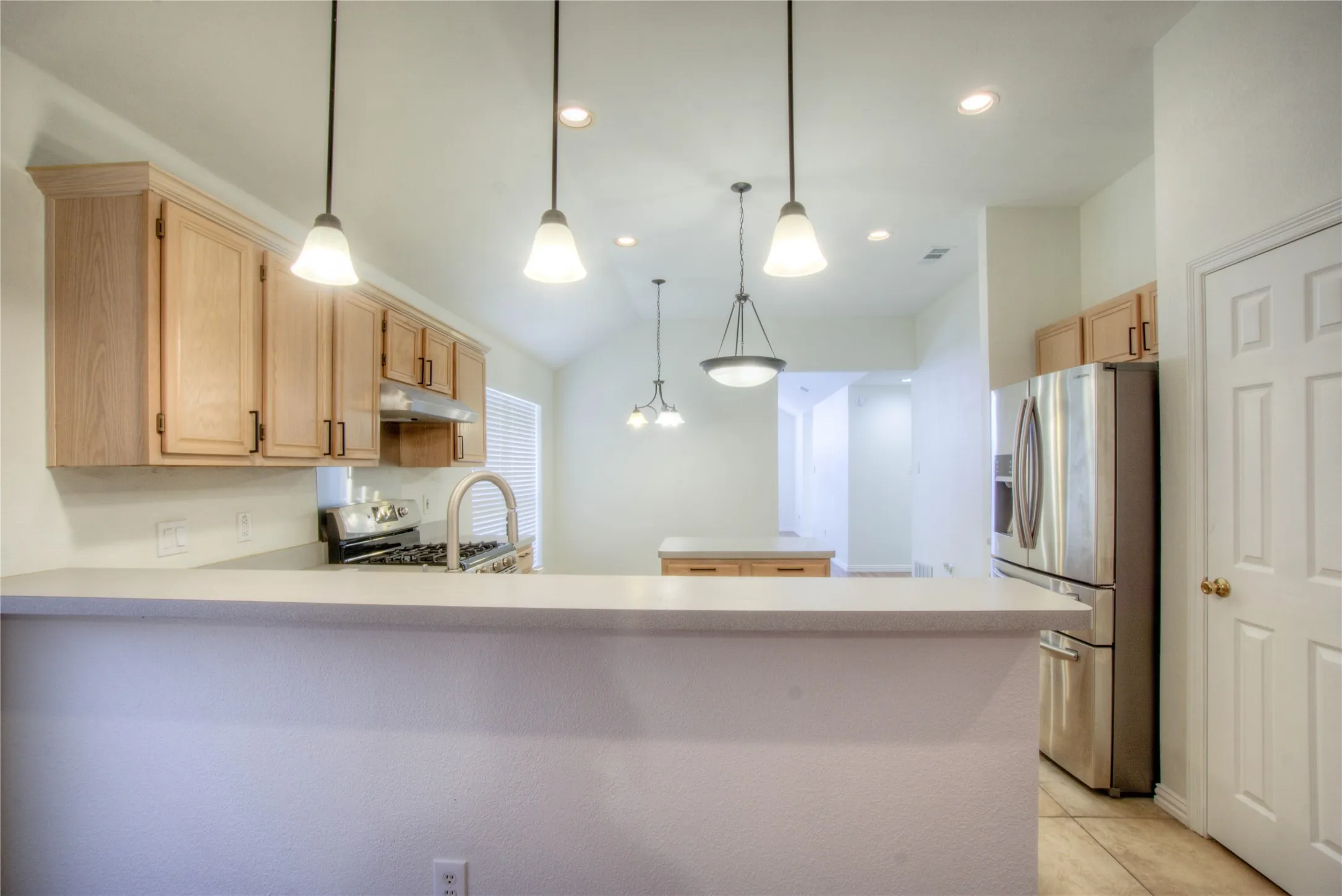 Kitchen featuring light wood cabinetry, stainless steel appliances, a white bar-height counter, and pendant lighting