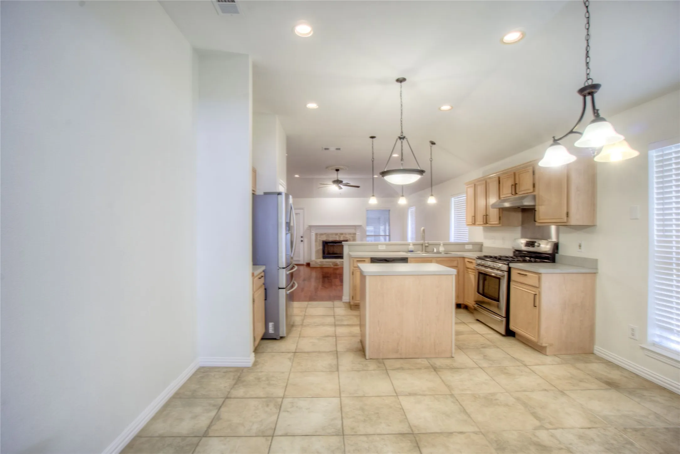 Kitchen featuring light wood-finish cabinetry, stainless steel appliances, a center island, and tile flooring