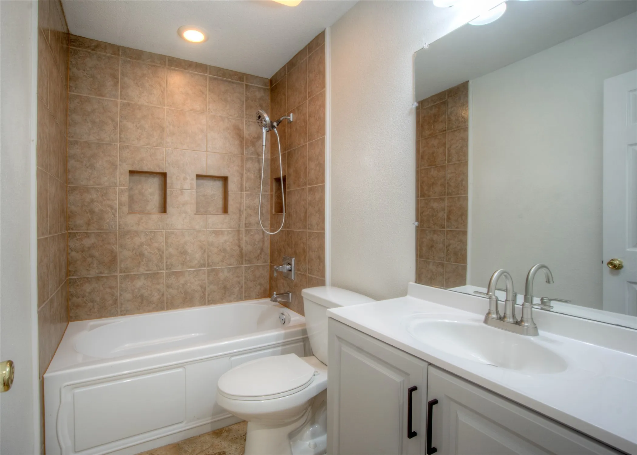 Full bath featuring a tub/shower combination with tile surround, dual built-in shower niches, and a vanity with an integrated sink and brushed nickel faucet