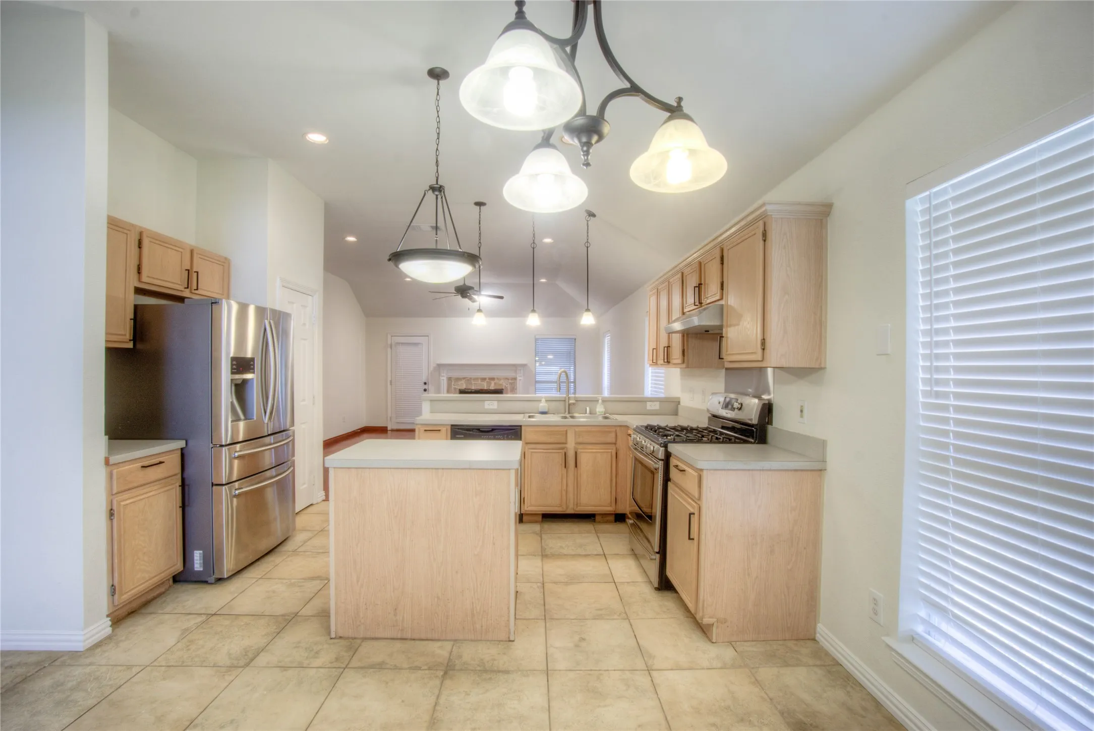 Kitchen featuring tile flooring, light wood-finish cabinetry, stainless steel appliances, a center island, and pendant lighting