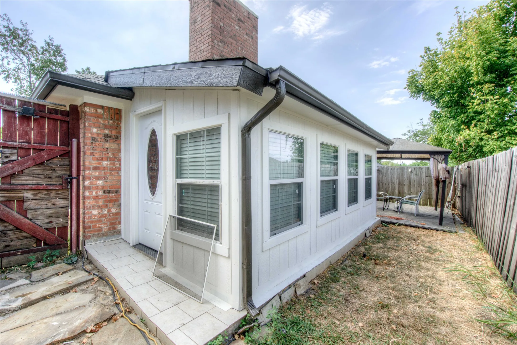 Brick exterior detailing, side entry door, multiple pane windows, privacy fencing, and a covered patio structure