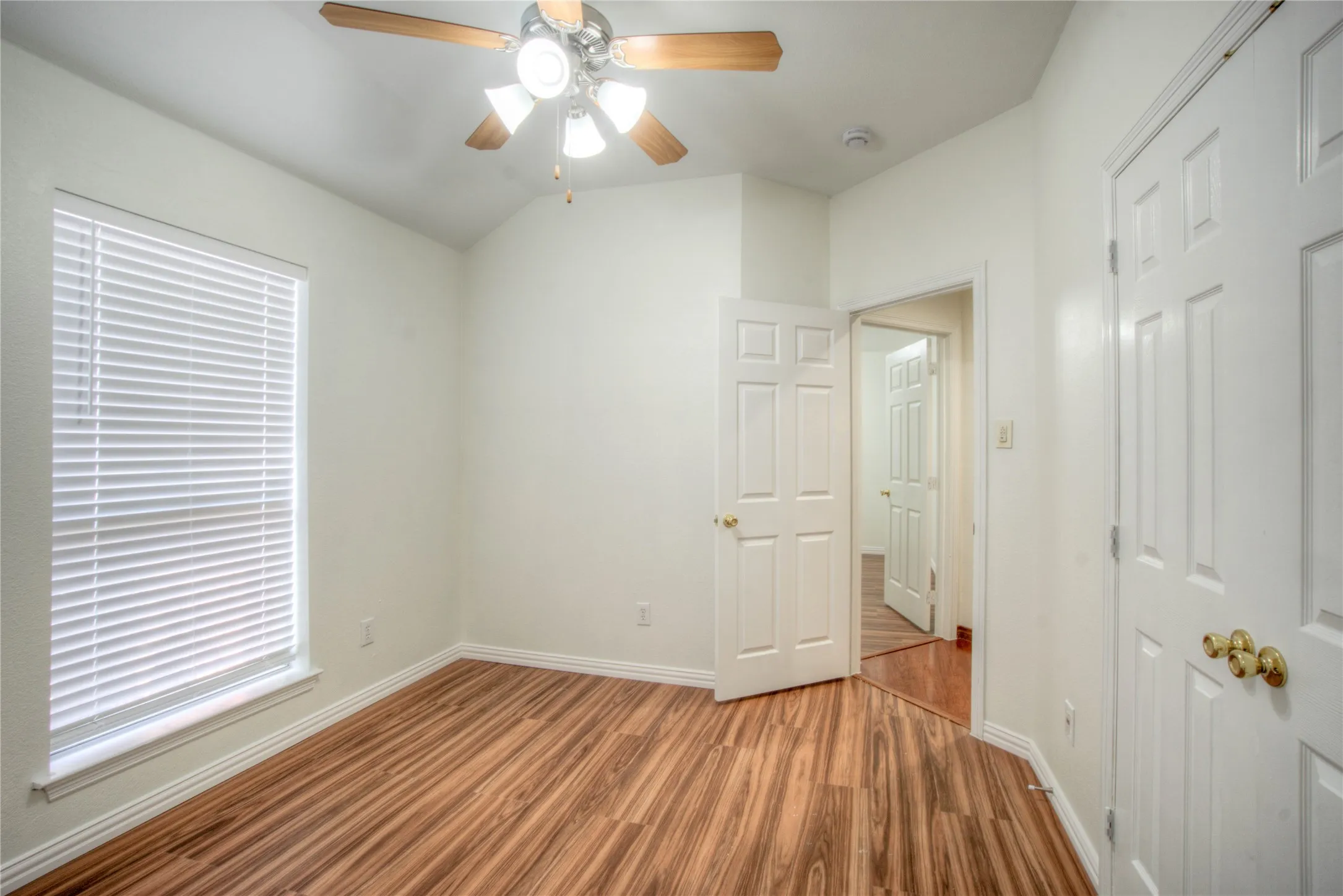 Wood-finish flooring, white walls, and a ceiling fan with integrated lighting