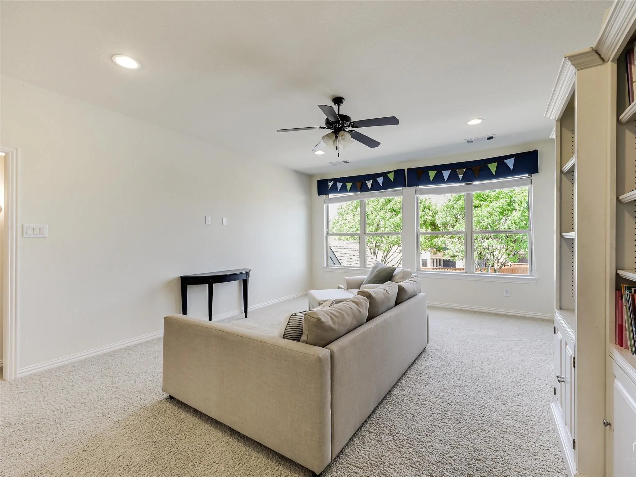 Recessed ceiling lighting, ceiling fan, carpet flooring, built-in shelving, and multiple windows
