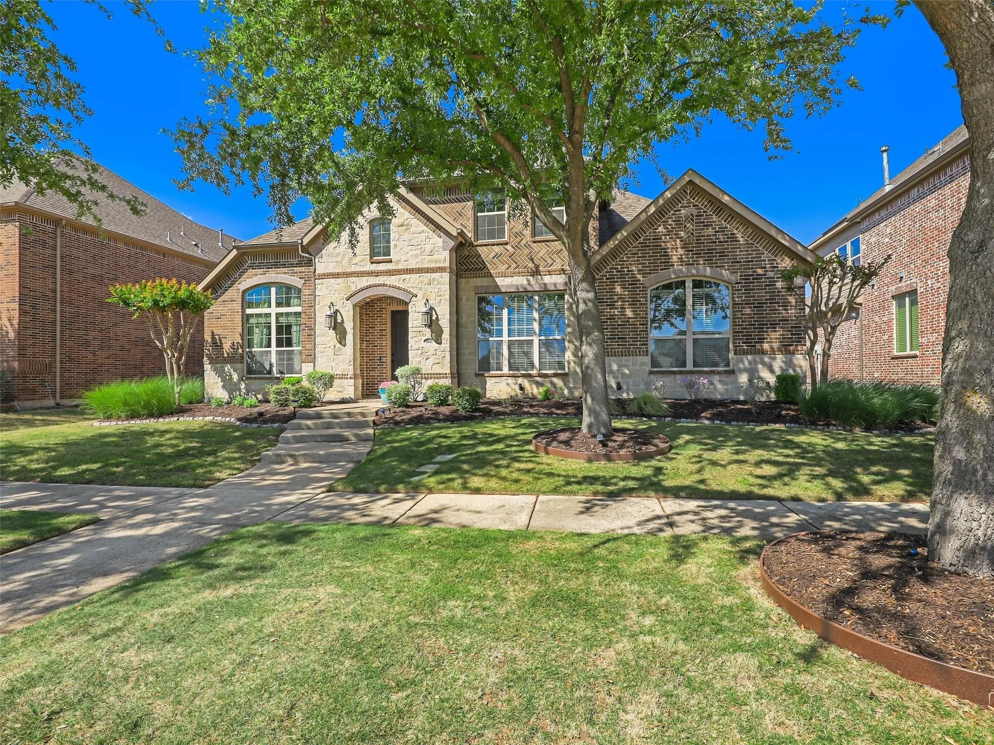 Brick and stone exterior featuring arched entry, decorative window accents, and established landscaping