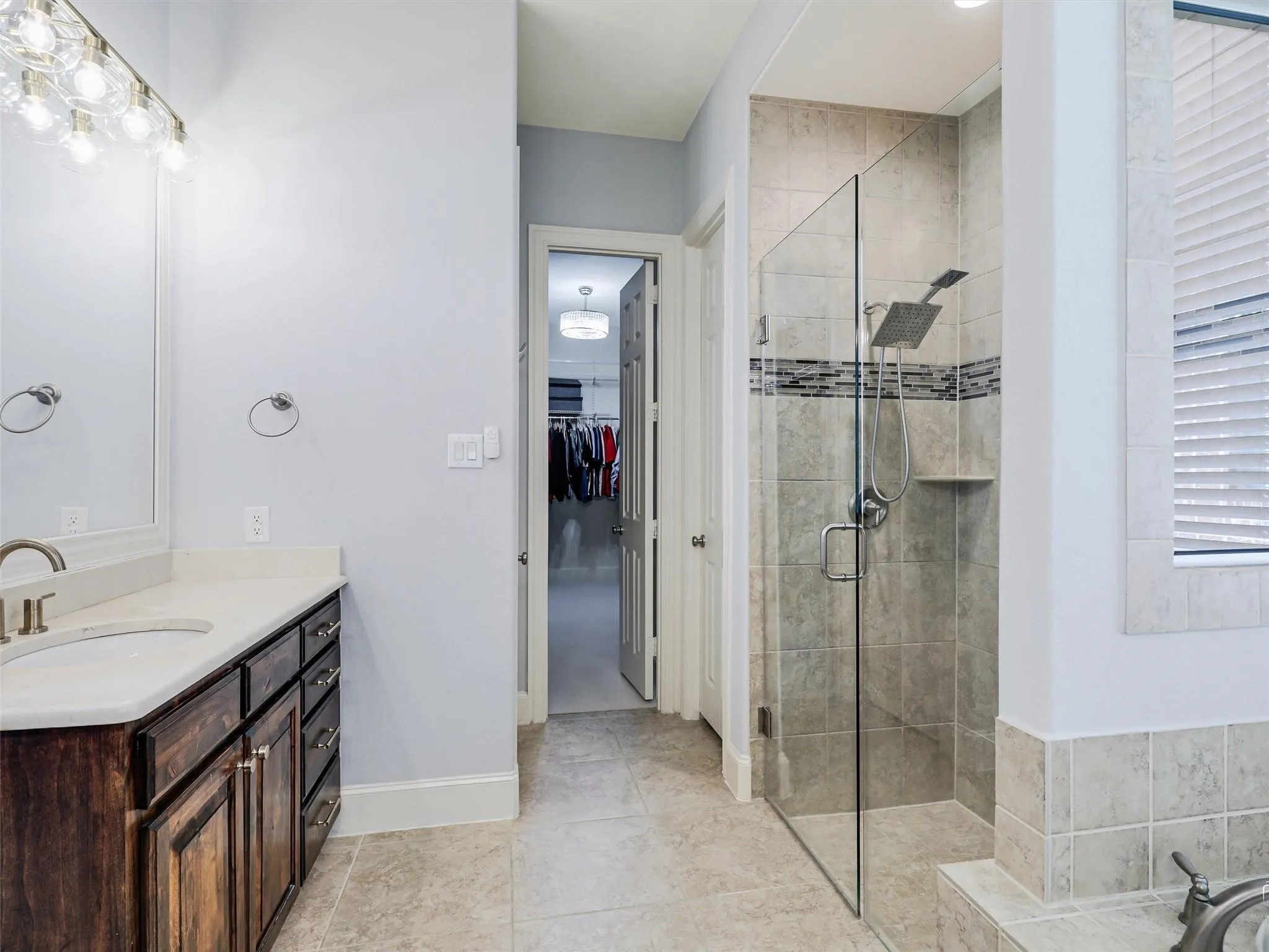 Spacious bathroom featuring a double vanity with stone countertop, wood-finish cabinetry, and a large walk-in shower with tile surround and glass enclosure
