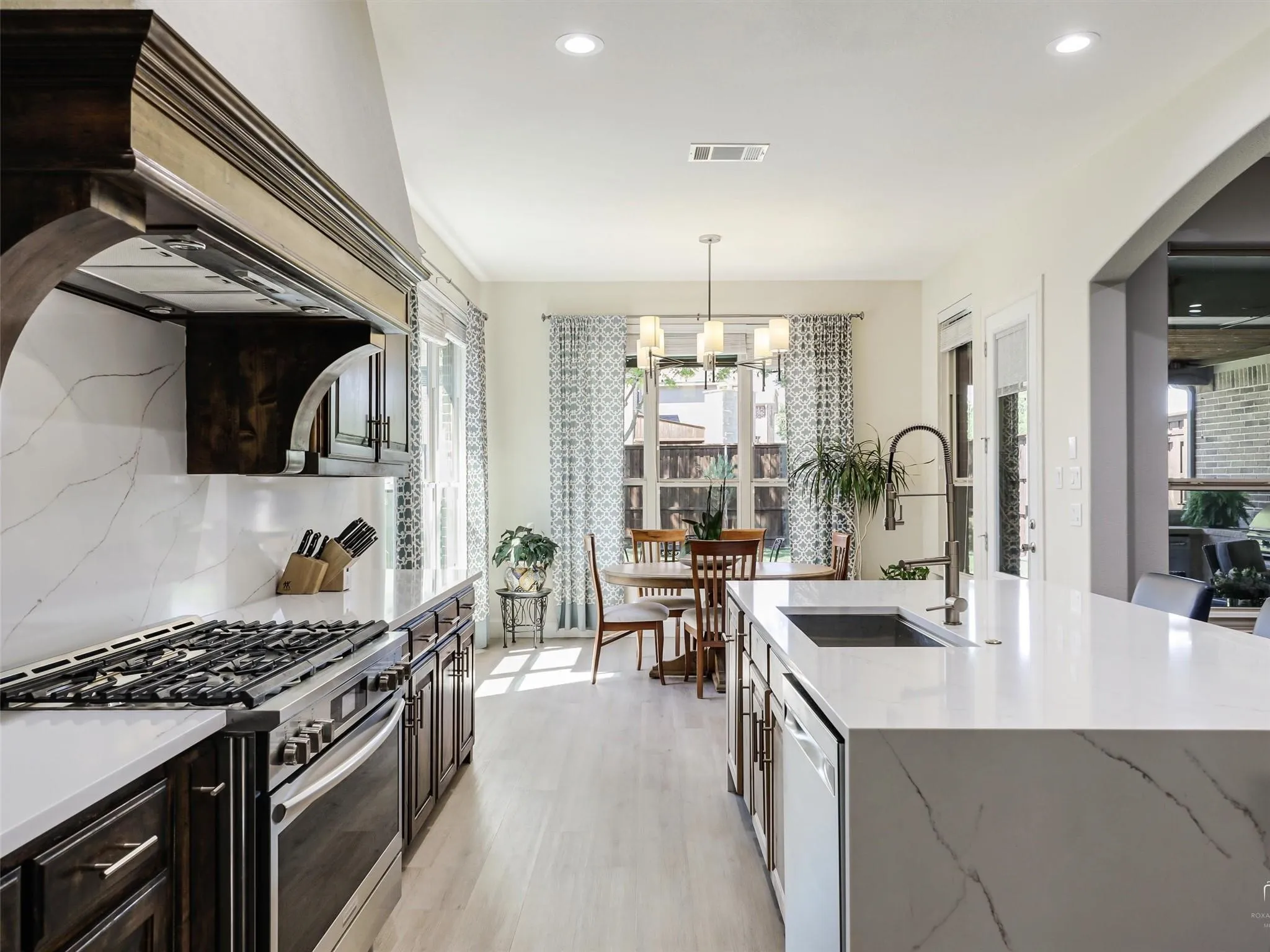 Kitchen featuring a gas range, stainless steel appliances, a large island with an undermount sink, recessed lighting, and light wood-finish flooring