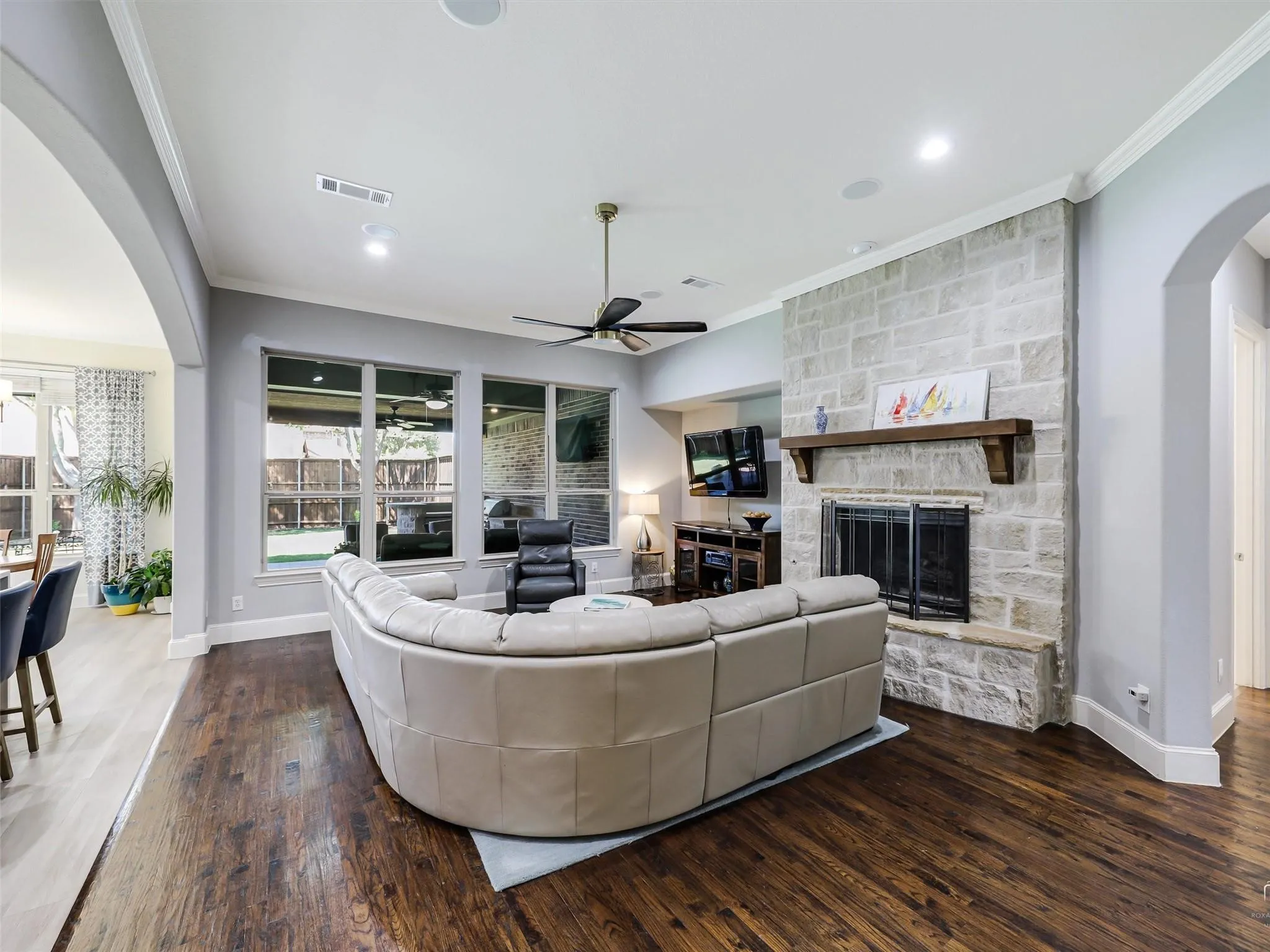 Spacious living area featuring rich wood-finish flooring, a stone-clad fireplace with a wood mantle, and a ceiling fan