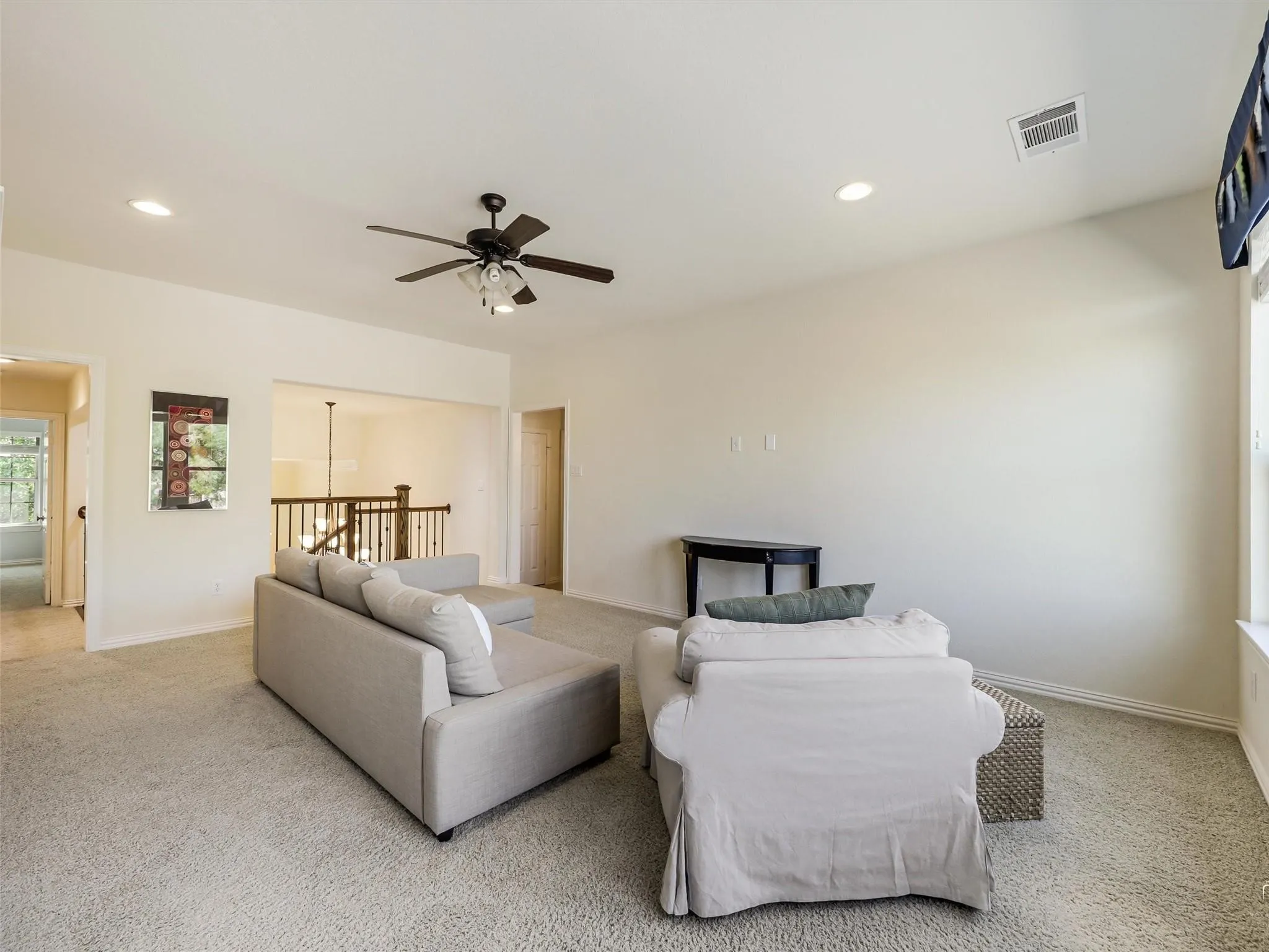 Carpeted living space featuring recessed lighting, a ceiling fan with light fixture, and a partial view of a wood-finish staircase railing