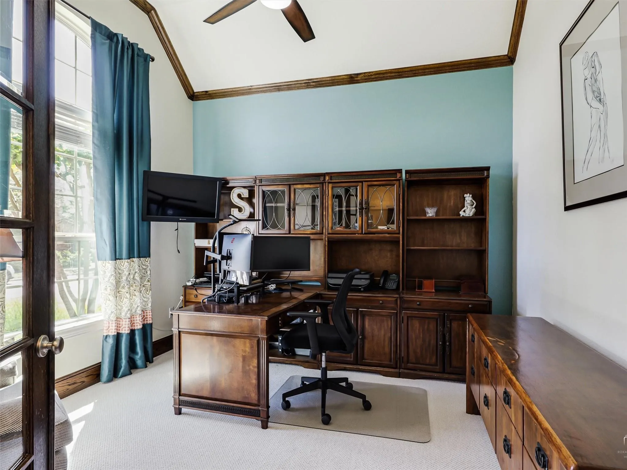 Arched entry door with glass panels, vaulted ceiling with wood beams, built-in dark wood cabinetry, and a ceiling fan