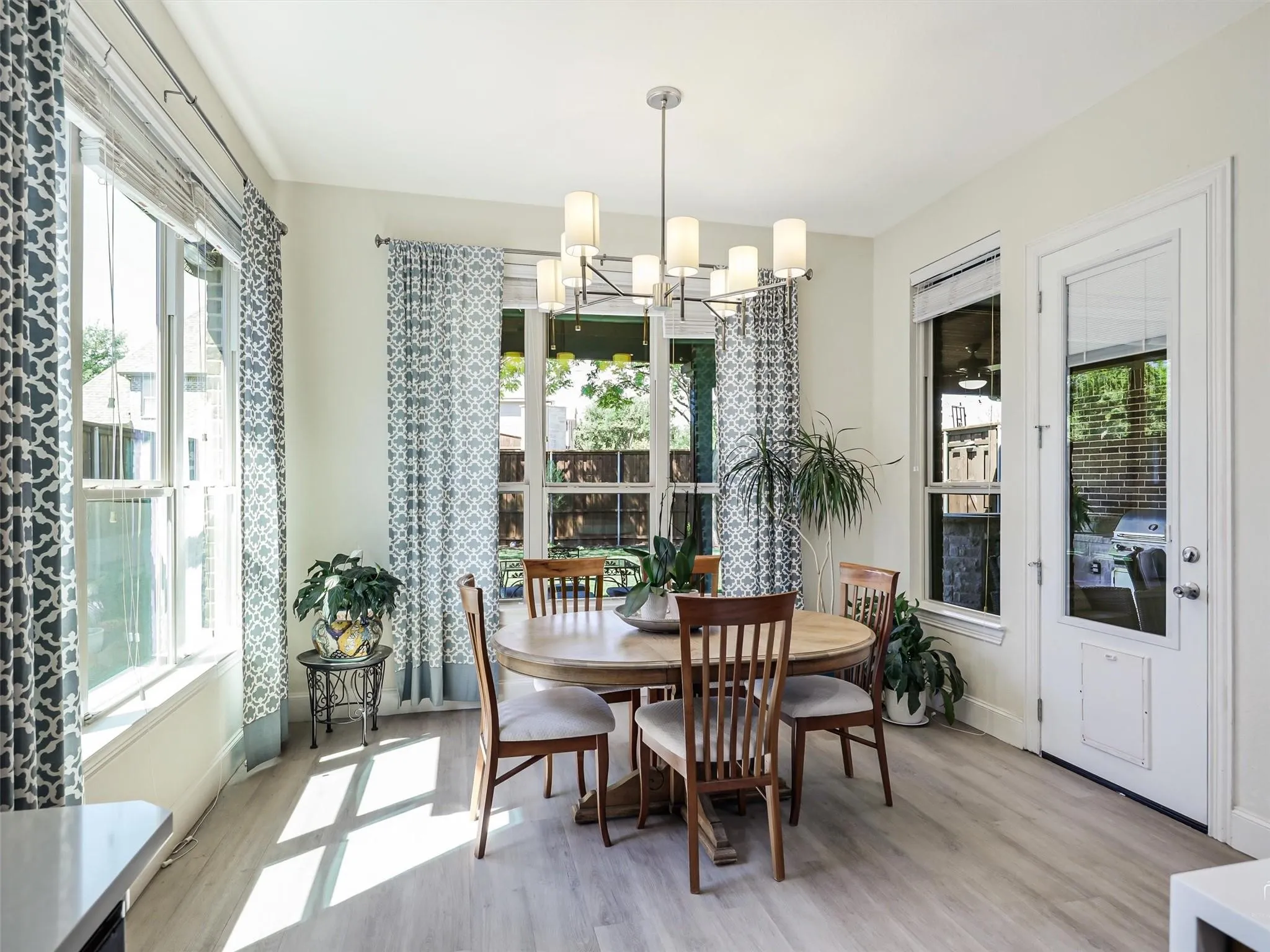 Spacious dining area featuring wood-finish flooring, a contemporary chandelier, multiple large windows, and a glass-paneled door
