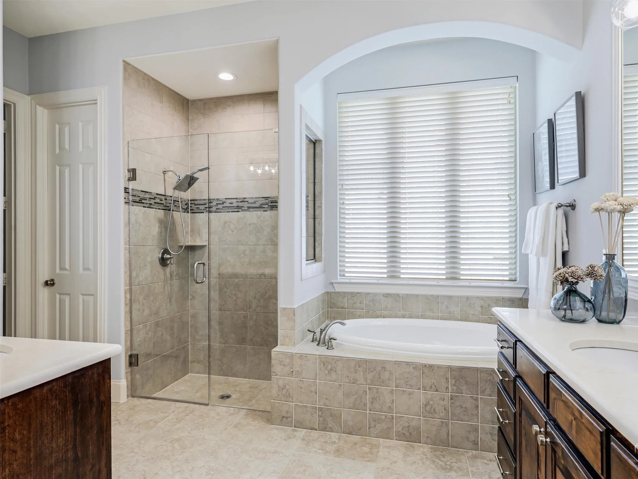 Tiled walk-in shower with a glass enclosure, separate soaking tub, and a dual vanity with a light-toned countertop
