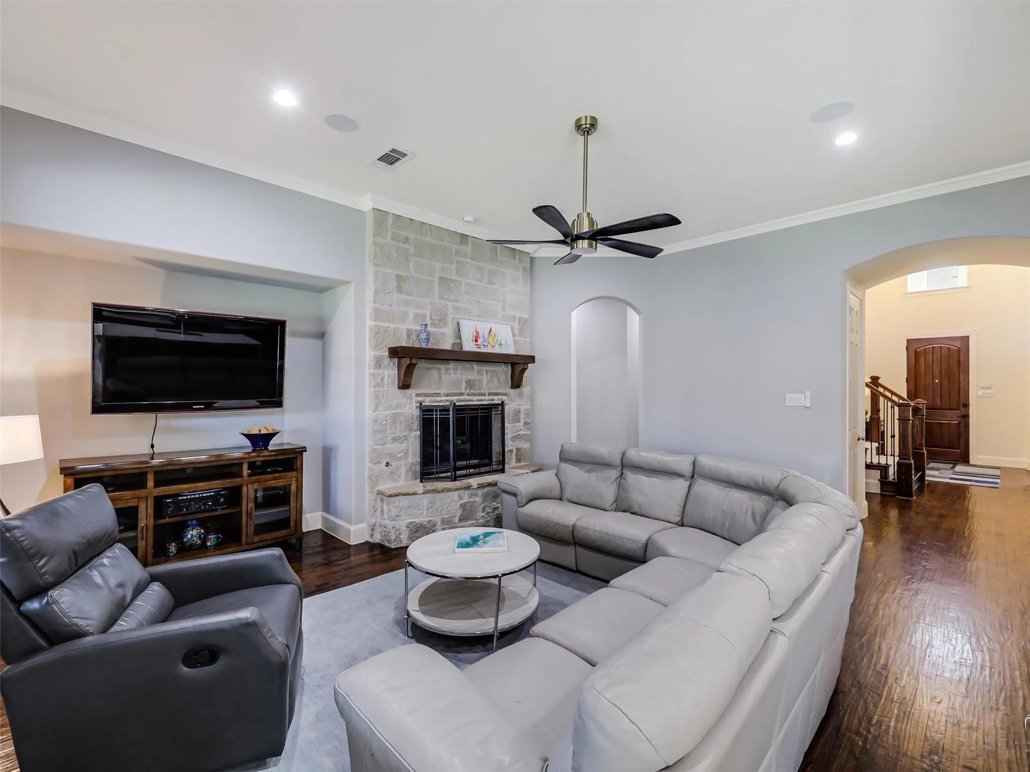 Hardwood flooring, stone-clad fireplace with wood mantel, ceiling fan with integrated lighting, recessed lighting, and crown molding