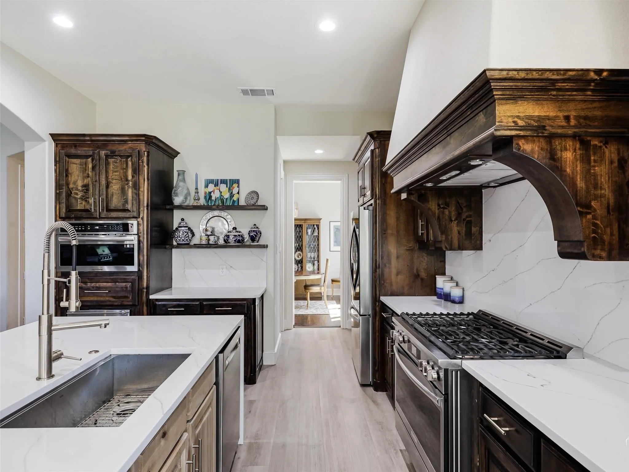 Gourmet kitchen featuring a built-in oven and microwave, stone countertops, a gas range with a custom wood hood, a large island with an undermount sink, and wood-finish flooring