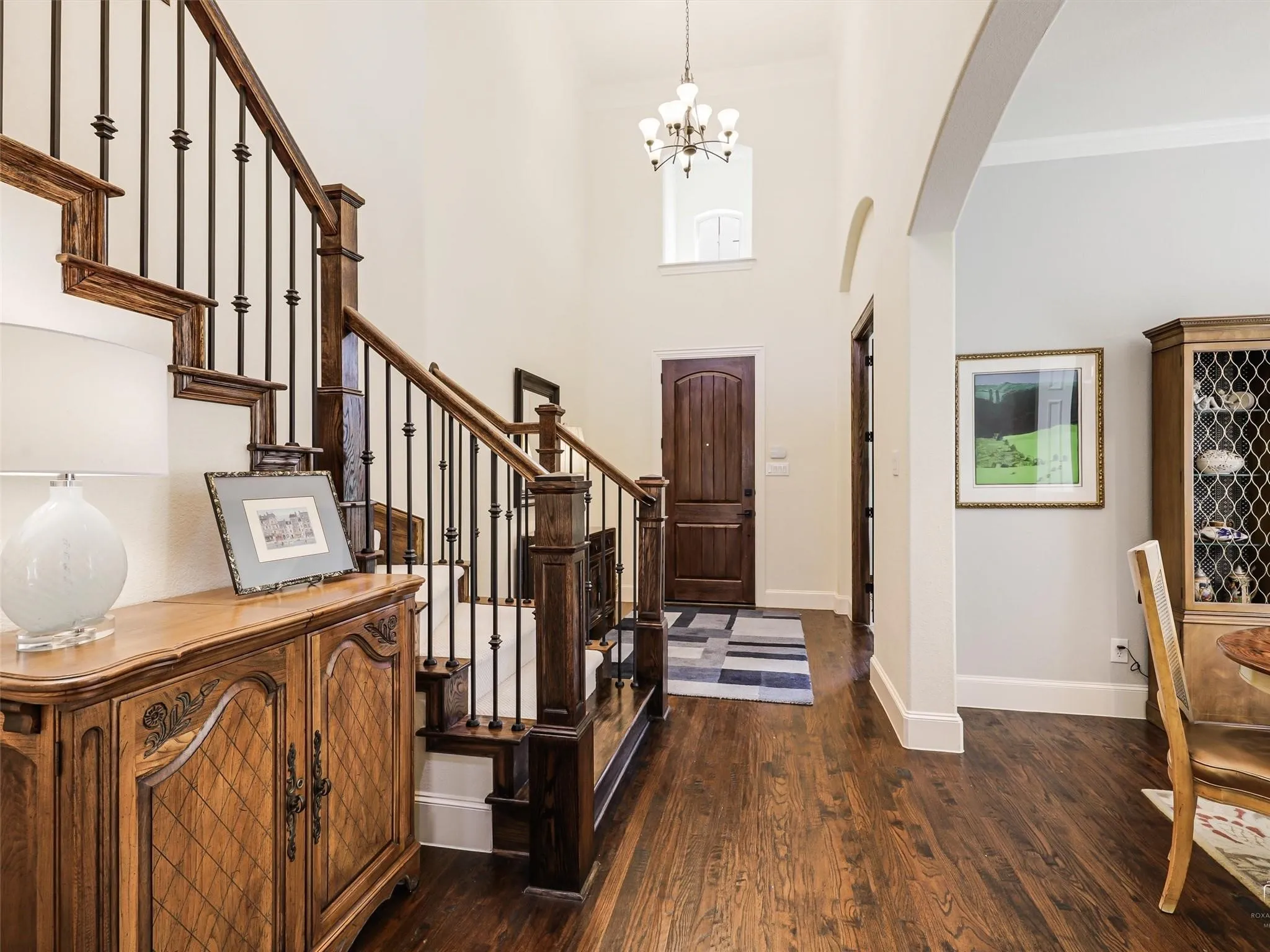 Wood-finish flooring throughout, wrought iron and wood staircase, arched doorways, and a double-height entryway with a chandelier
