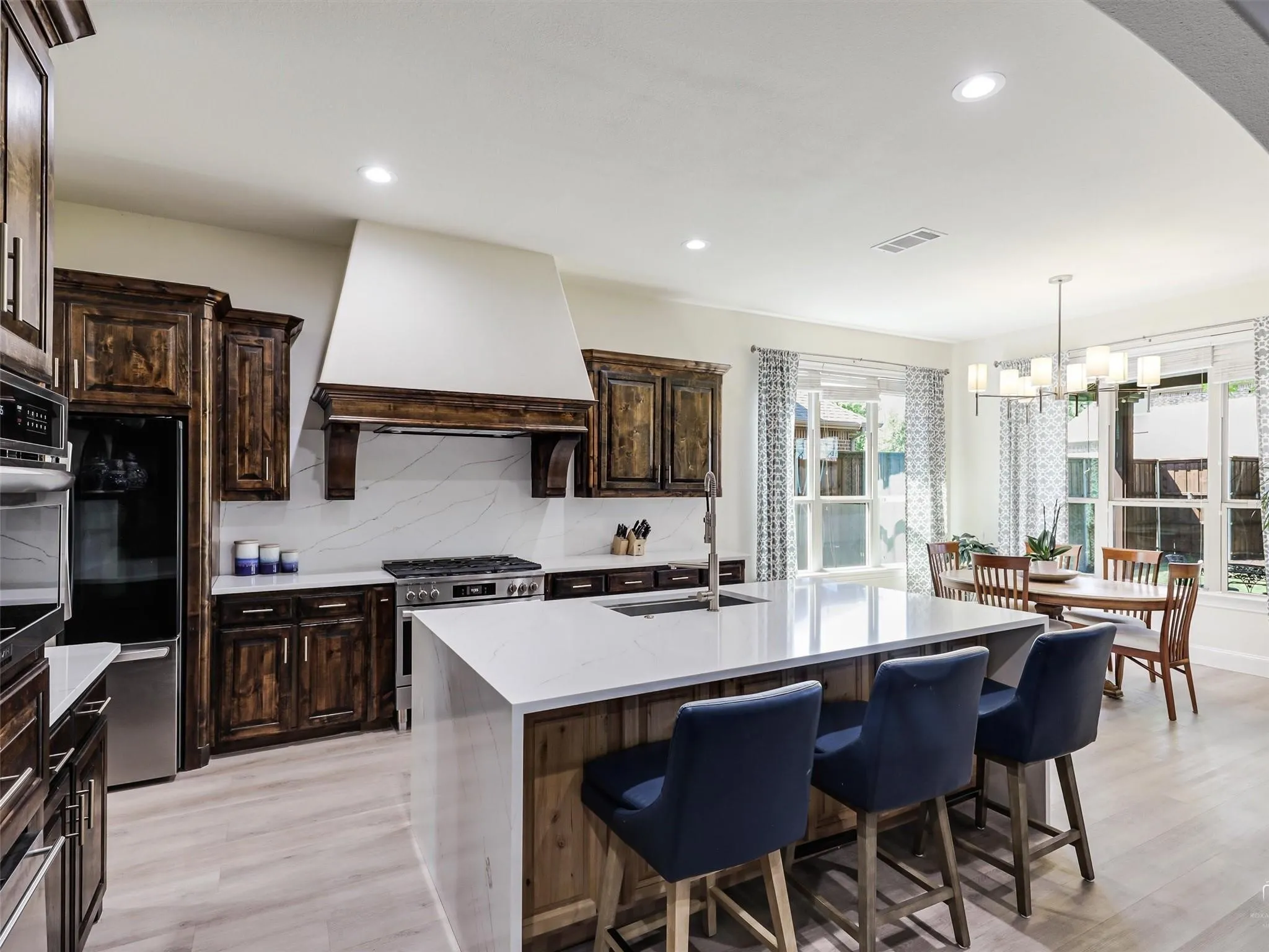 Expansive kitchen featuring wood-finish cabinetry, stainless steel appliances, a center island with countertop seating, and recessed lighting