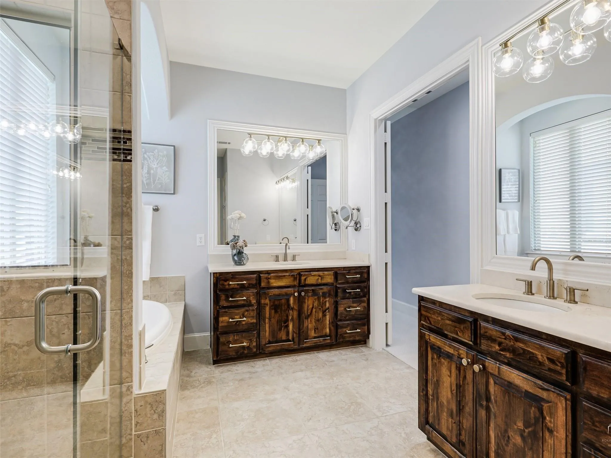 Dual wood-finish vanities with light countertops, separate shower with glass enclosure, soaking tub, and tiled flooring