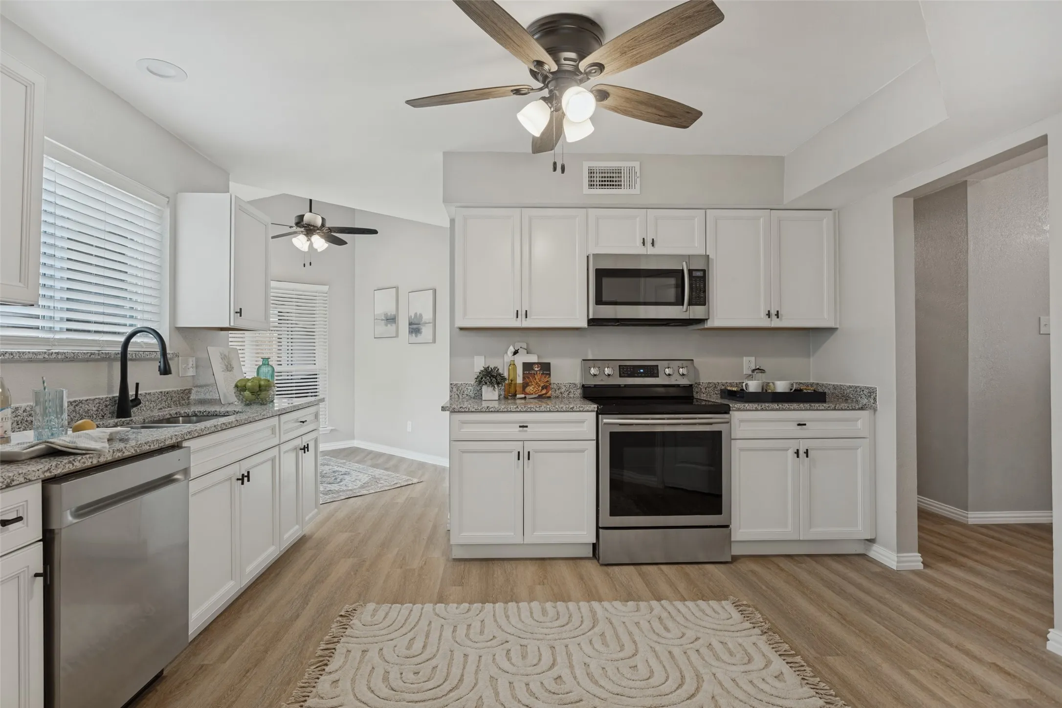 Kitchen featuring new white cabinetry, granite countertops, stainless steel appliances, wood-finish flooring, and ceiling fans.