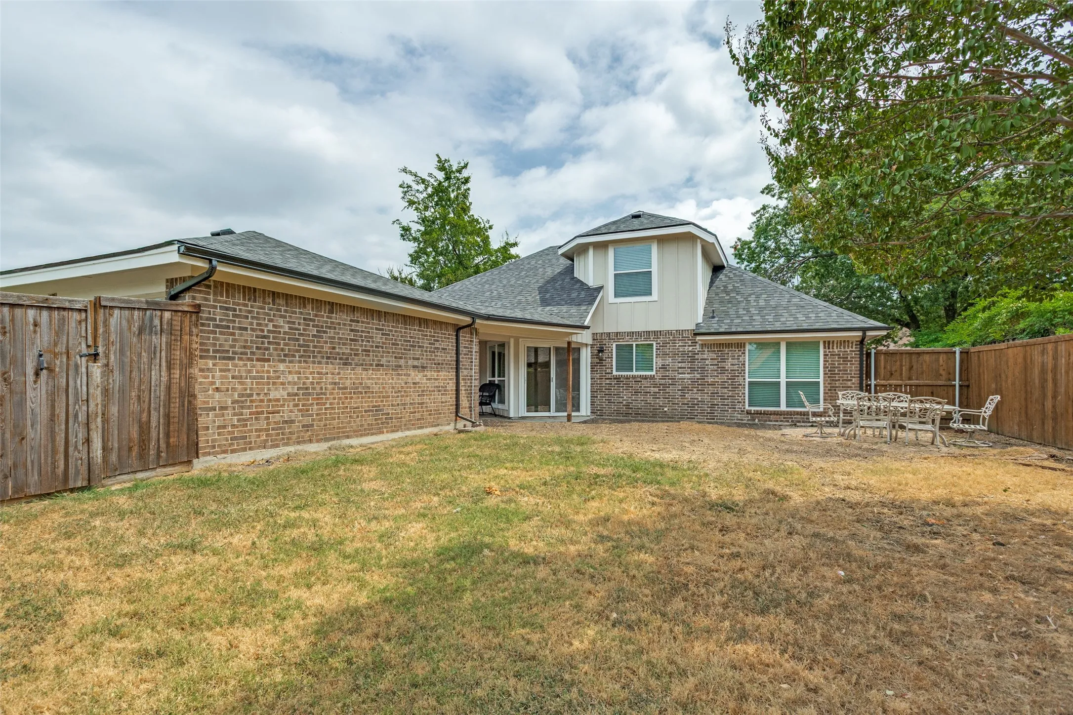 Expansive backyard with a brick and siding exterior, a wood privacy fence, and a patio area