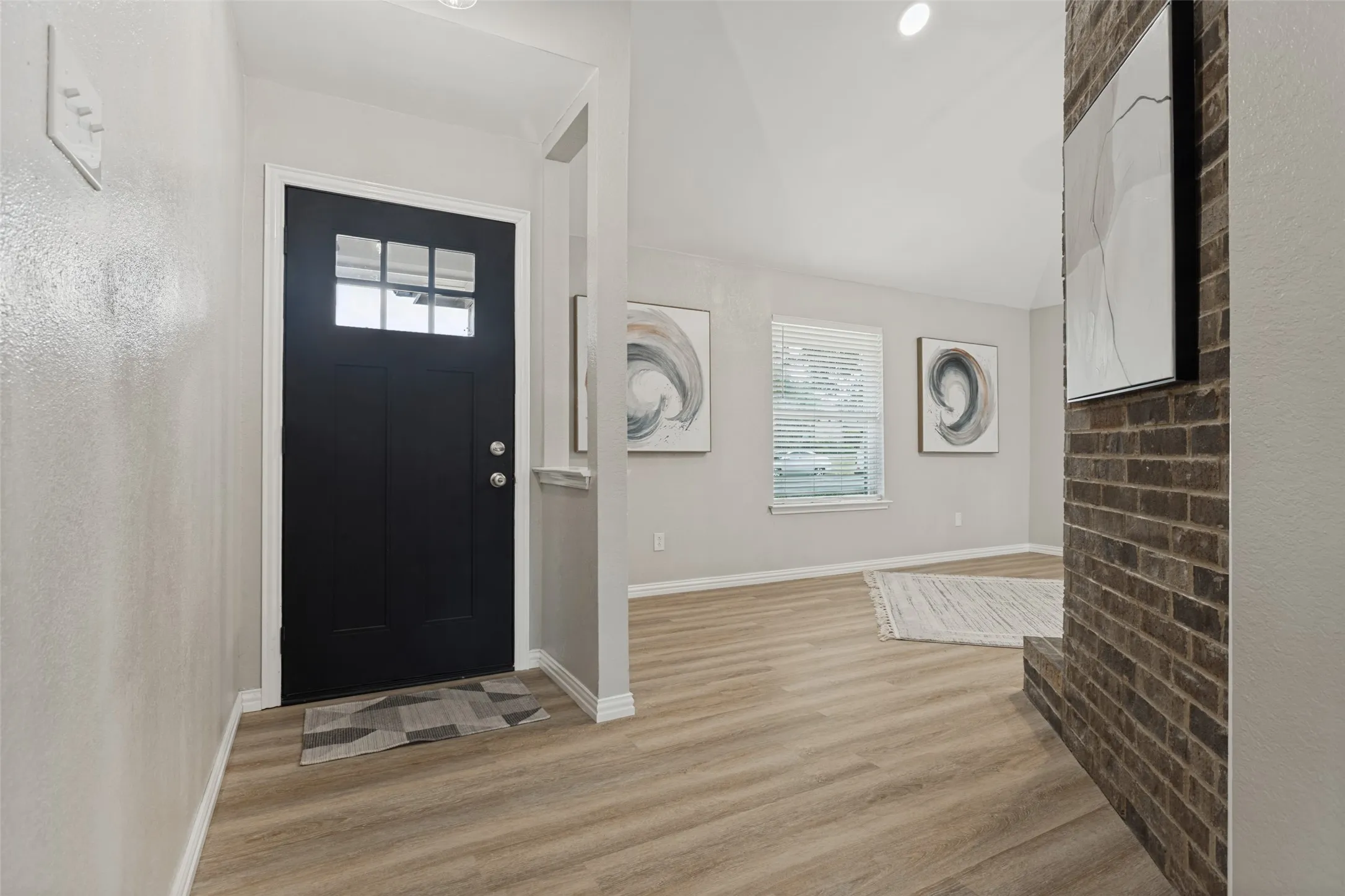 Entryway with a black paneled door featuring multiple glass panes, complemented by wood-finish flooring extending into the adjacent living space