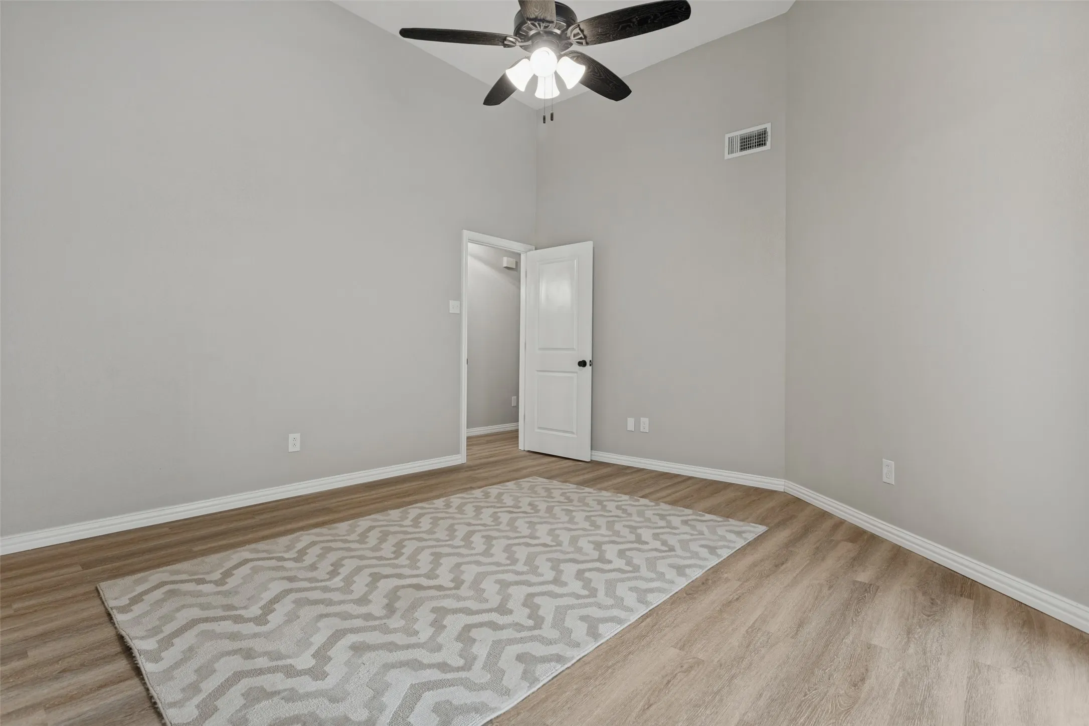 Vaulted ceiling with a ceiling fan, light-toned wood-finish flooring, and crisp white trim