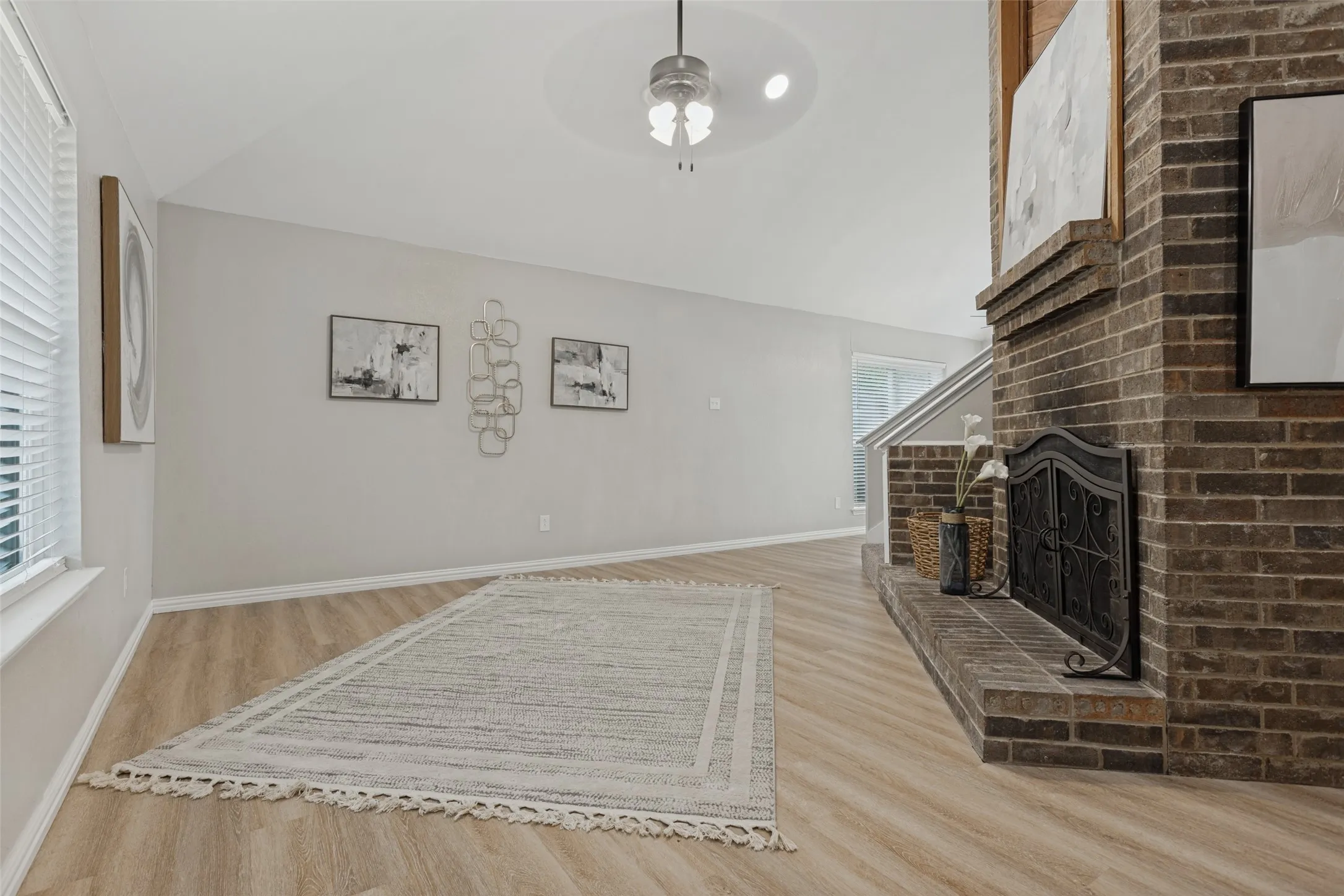 Vaulted ceiling with a ceiling fan, brick fireplace with a hearth, and new luxury vinyl plank flooring.