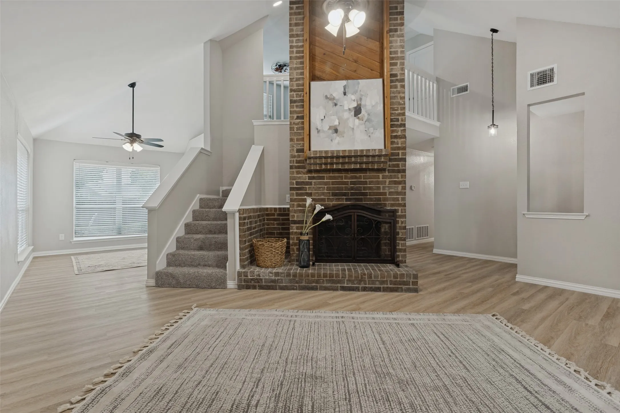 Vaulted ceiling living space featuring a brick fireplace with wood paneling, wood-finish flooring, and a carpeted staircase with white railings