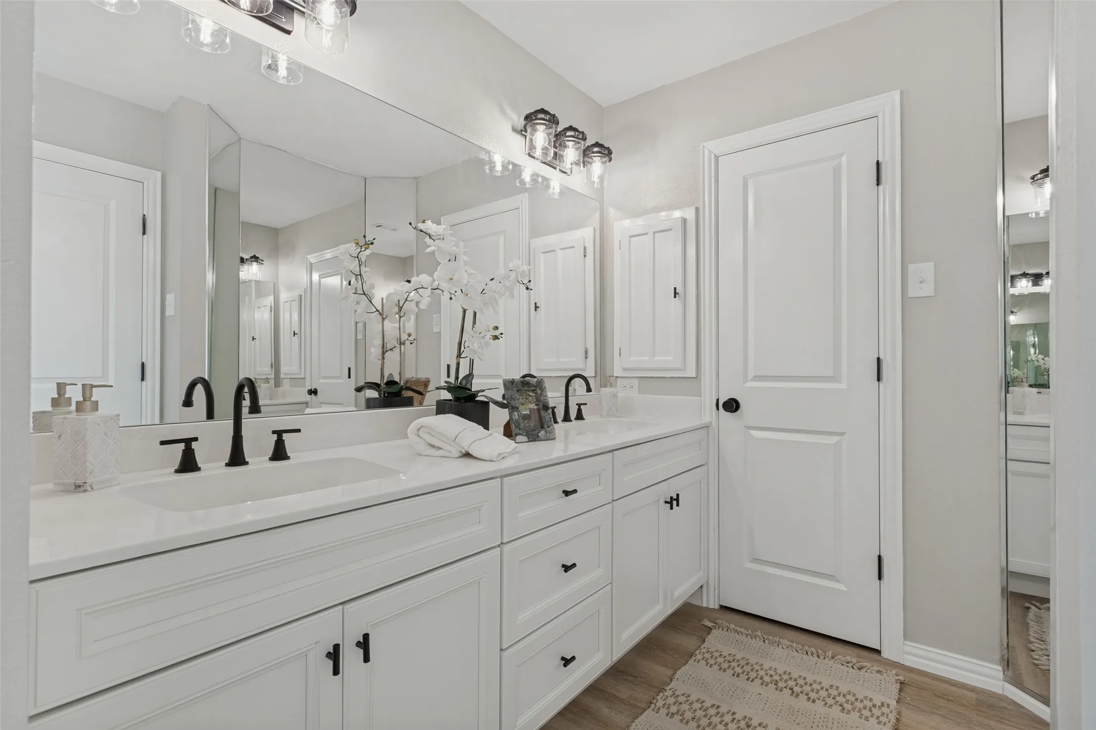 Dual vanity with white cabinetry, matte black fixtures, integrated sinks, and a full-width wall mirror