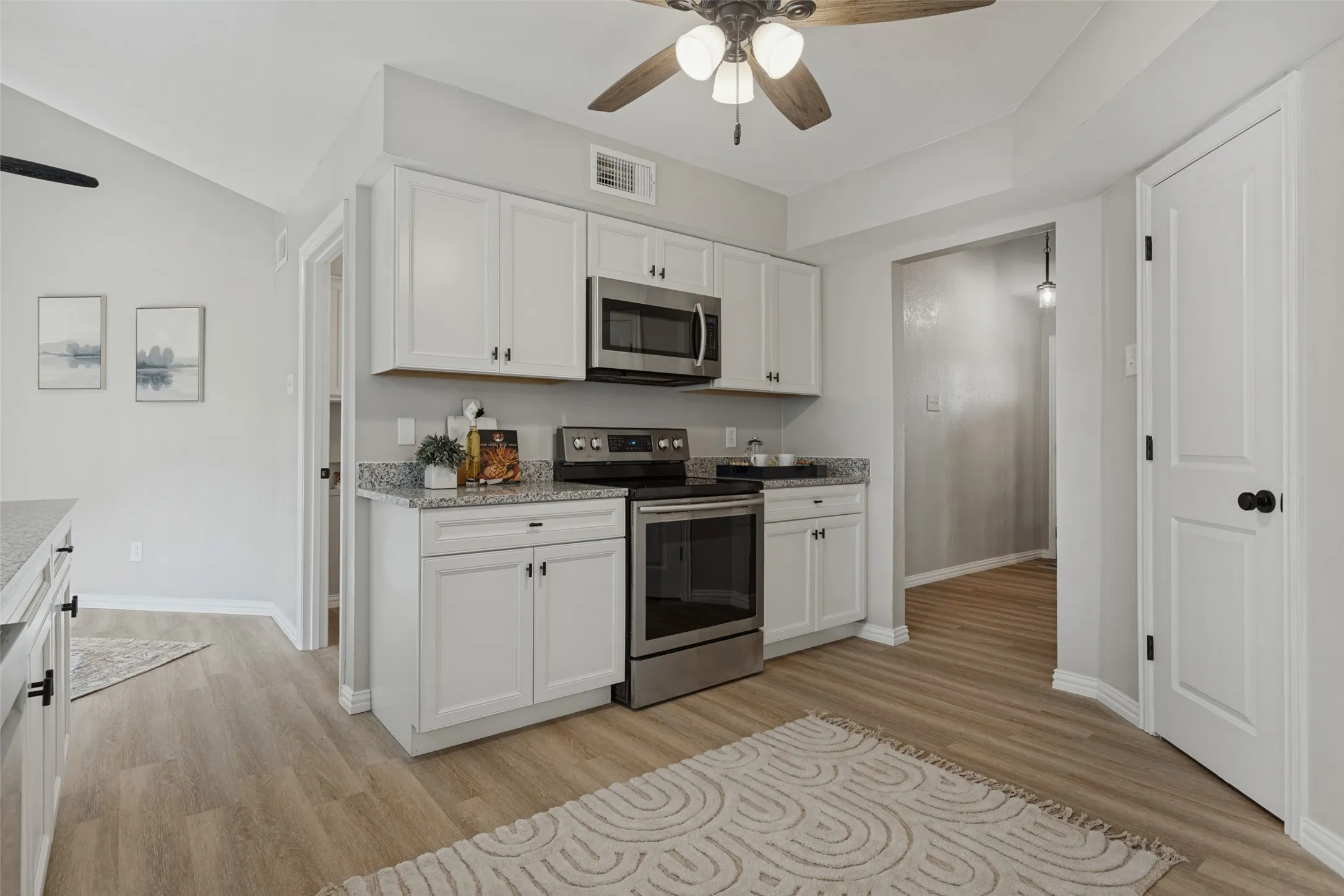 Kitchen featuring new white shaker cabinetry, stainless steel appliances, granite-style countertops, wood-finish flooring, and a ceiling fan