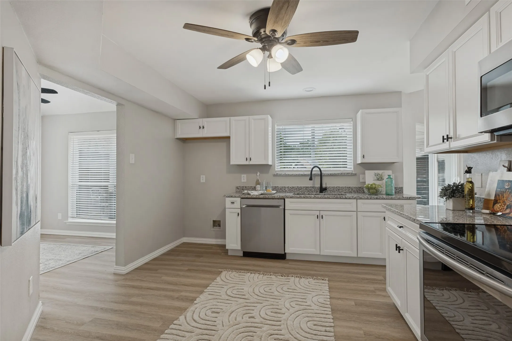 Kitchen featuring white cabinetry, wood-finish flooring, stainless steel appliances, and a ceiling fan with integrated lighting