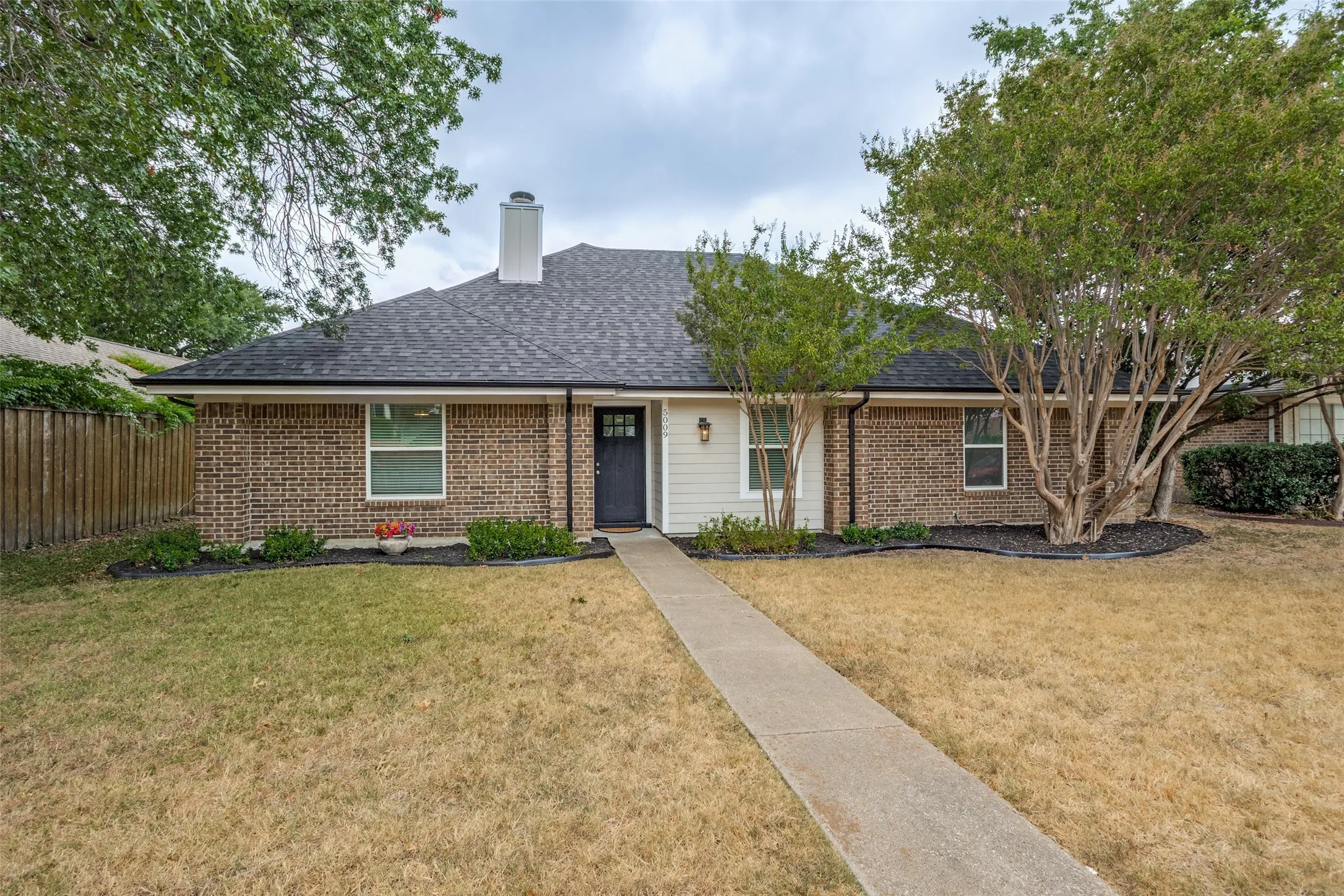 Brick exterior with white siding accents, dark roof, front entry door, and a concrete walkway