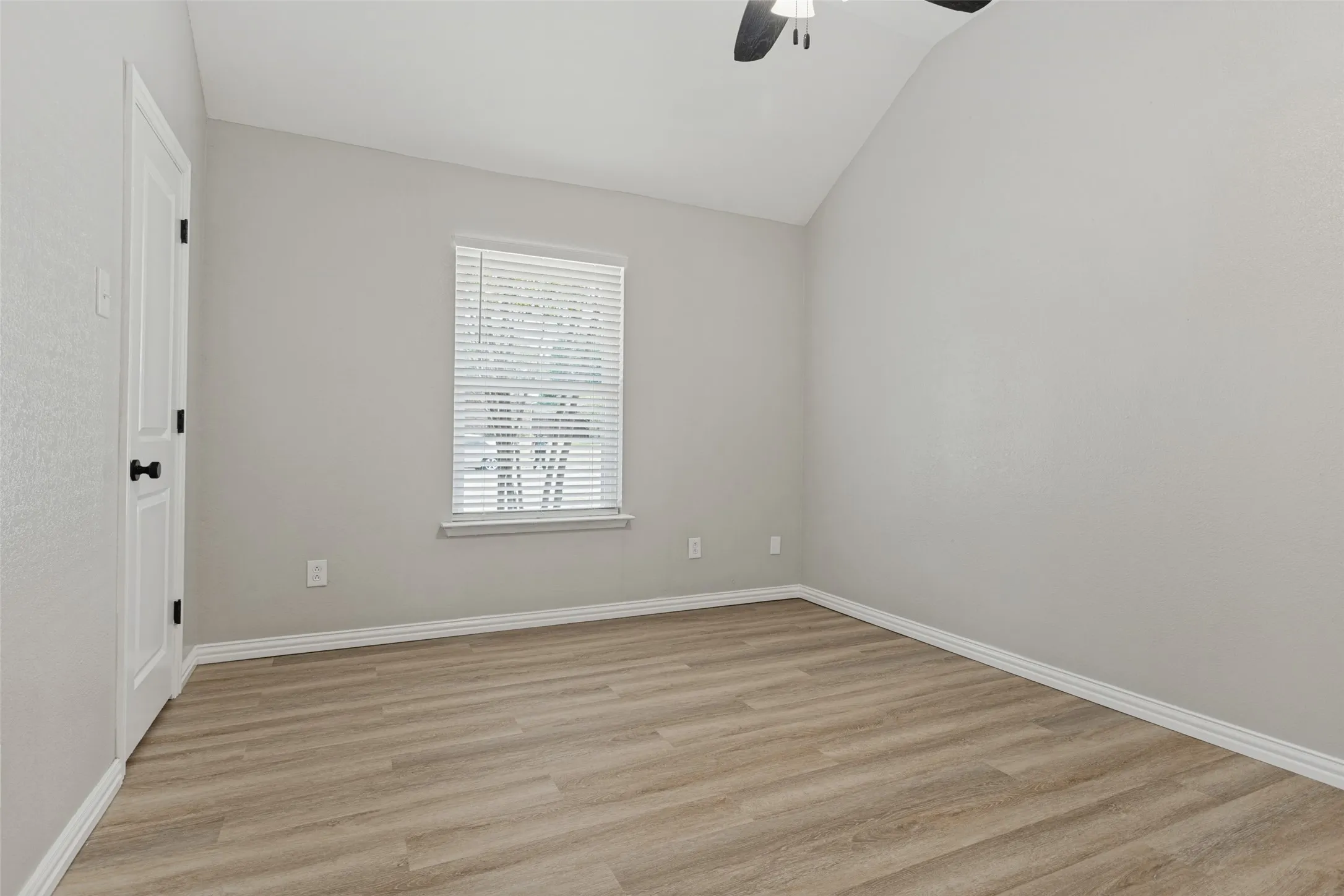 Secondary bedroom with vaulted ceiling, a lighted ceiling fan, wood-finish flooring, and white window blinds.