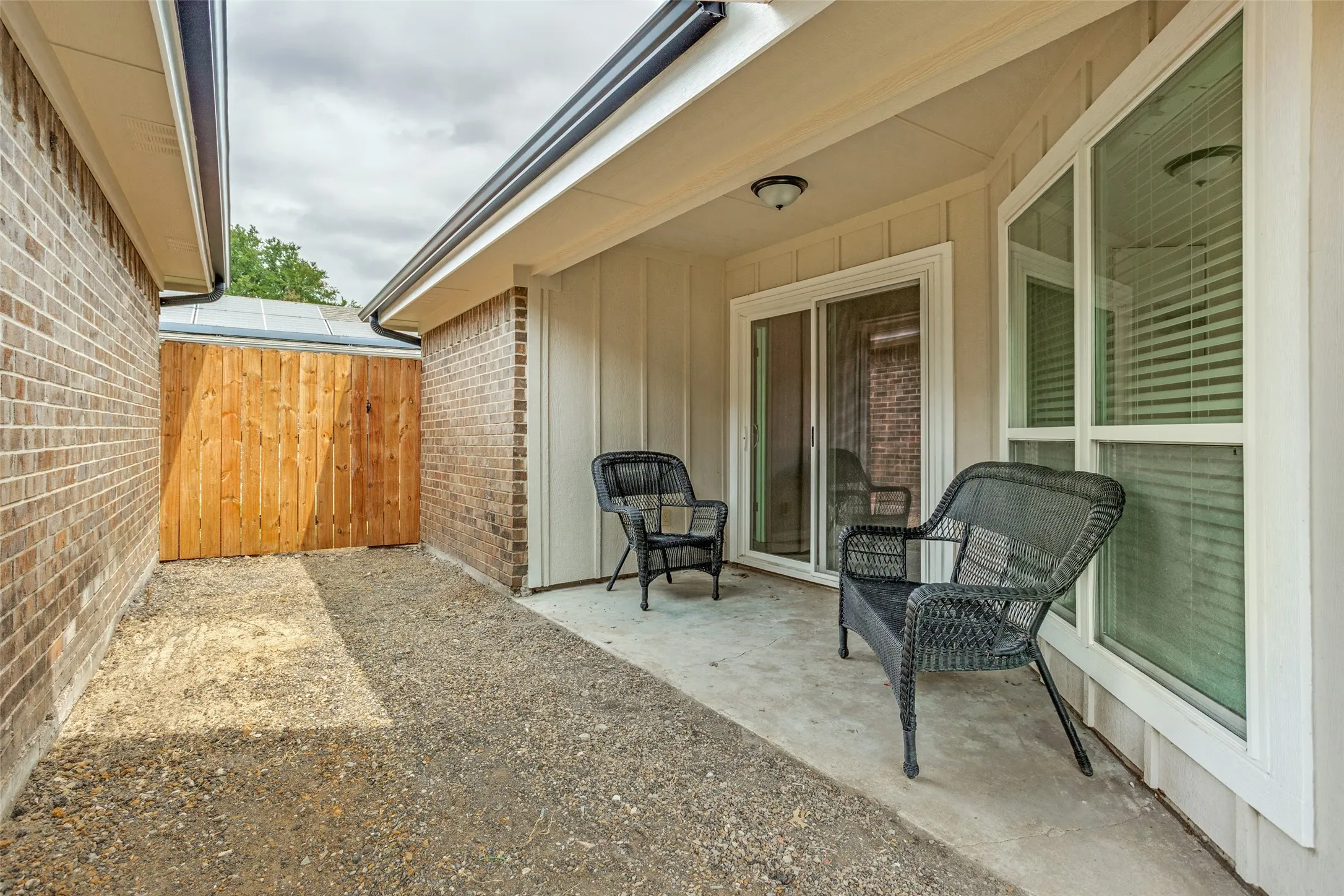 Covered patio with a concrete surface, featuring an exterior light fixture, sliding glass door, and a multi-pane window