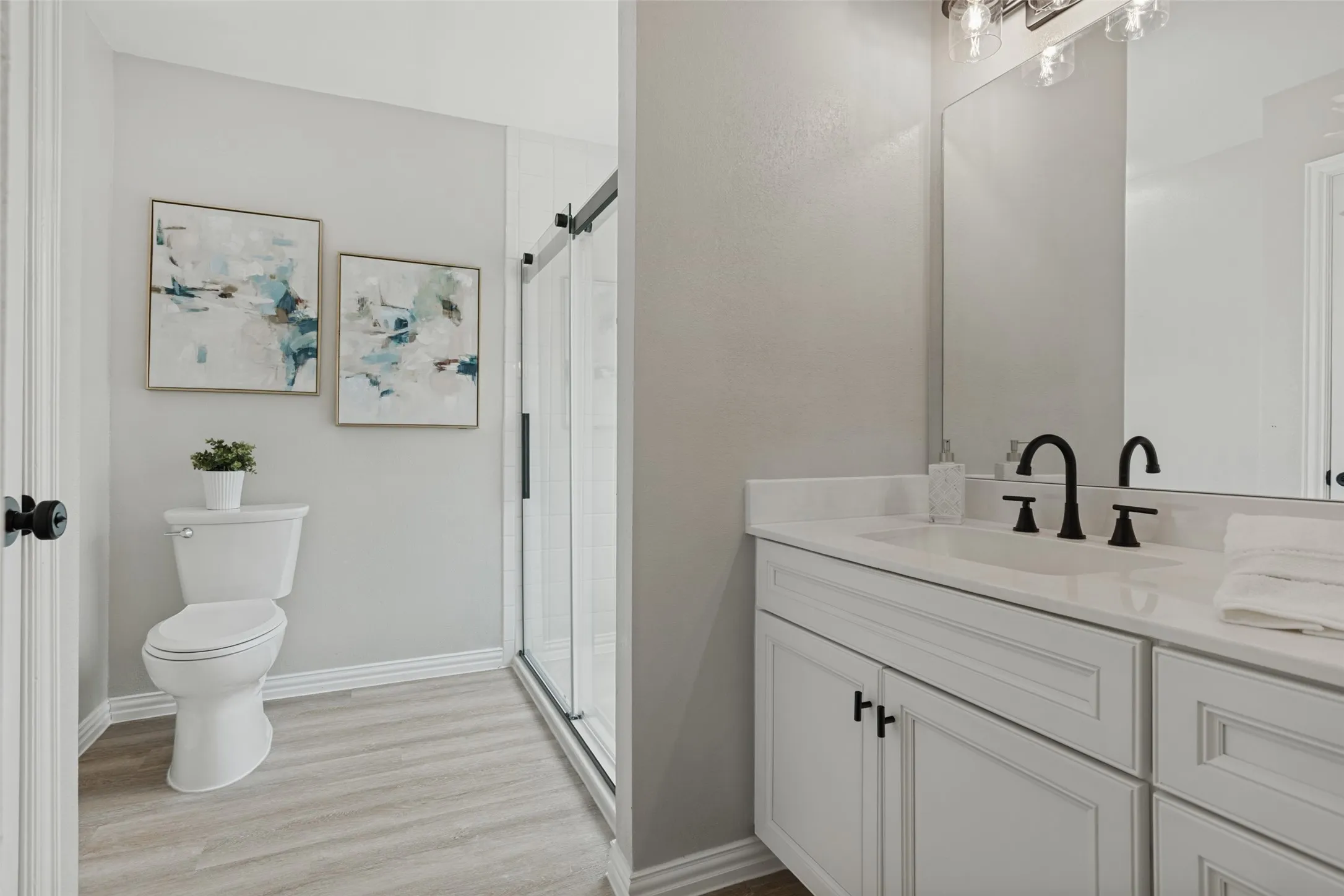 White vanity with a quartz countertop, black fixtures, and a clear glass shower enclosure