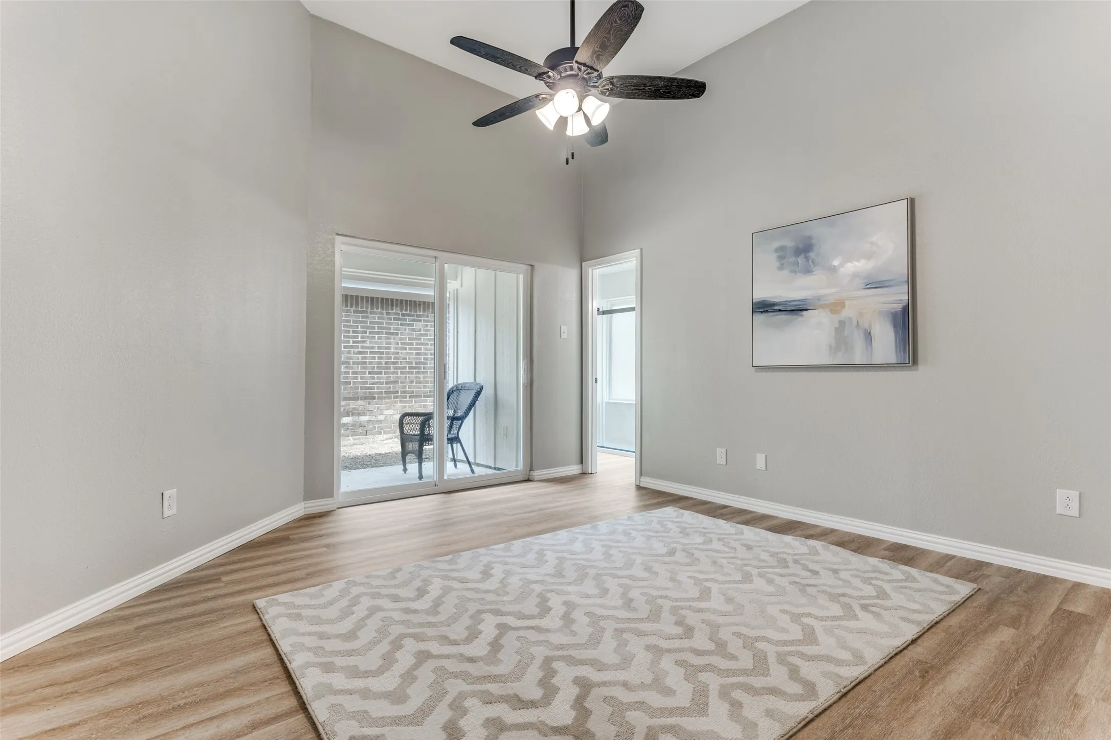 Primary bedroom with high ceilings, lighted ceiling fan, new luxury vinyl plank flooring and open to patio.