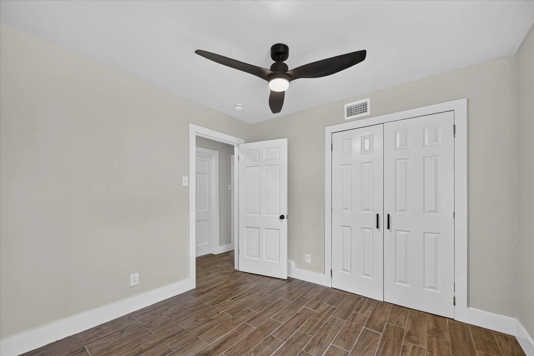 Wood-finish flooring, light gray wall tones, white trim, and a ceiling fan with integrated lighting