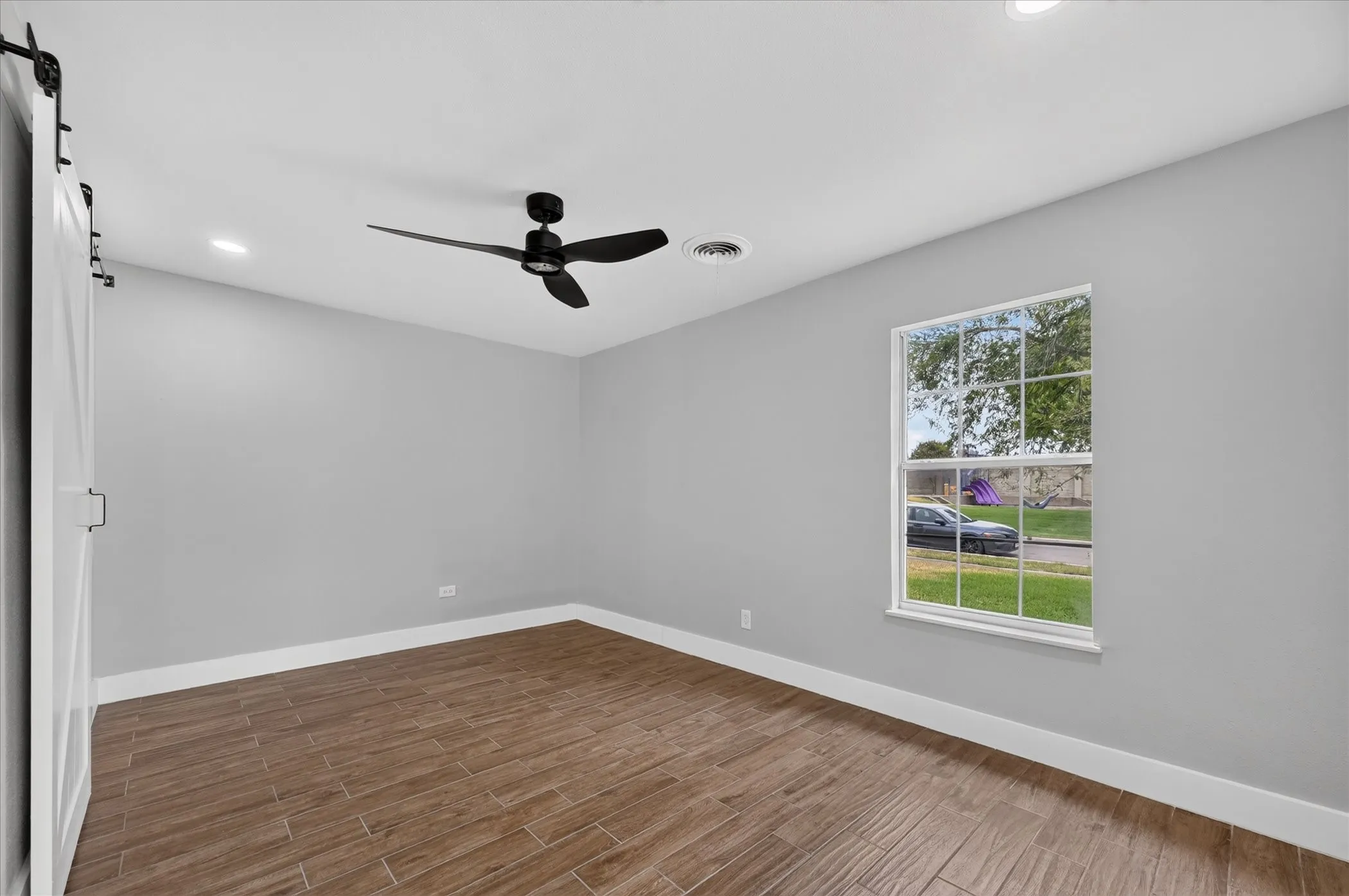 Wood-finish tile flooring, recessed lighting, ceiling fan, white barn door, and a single window