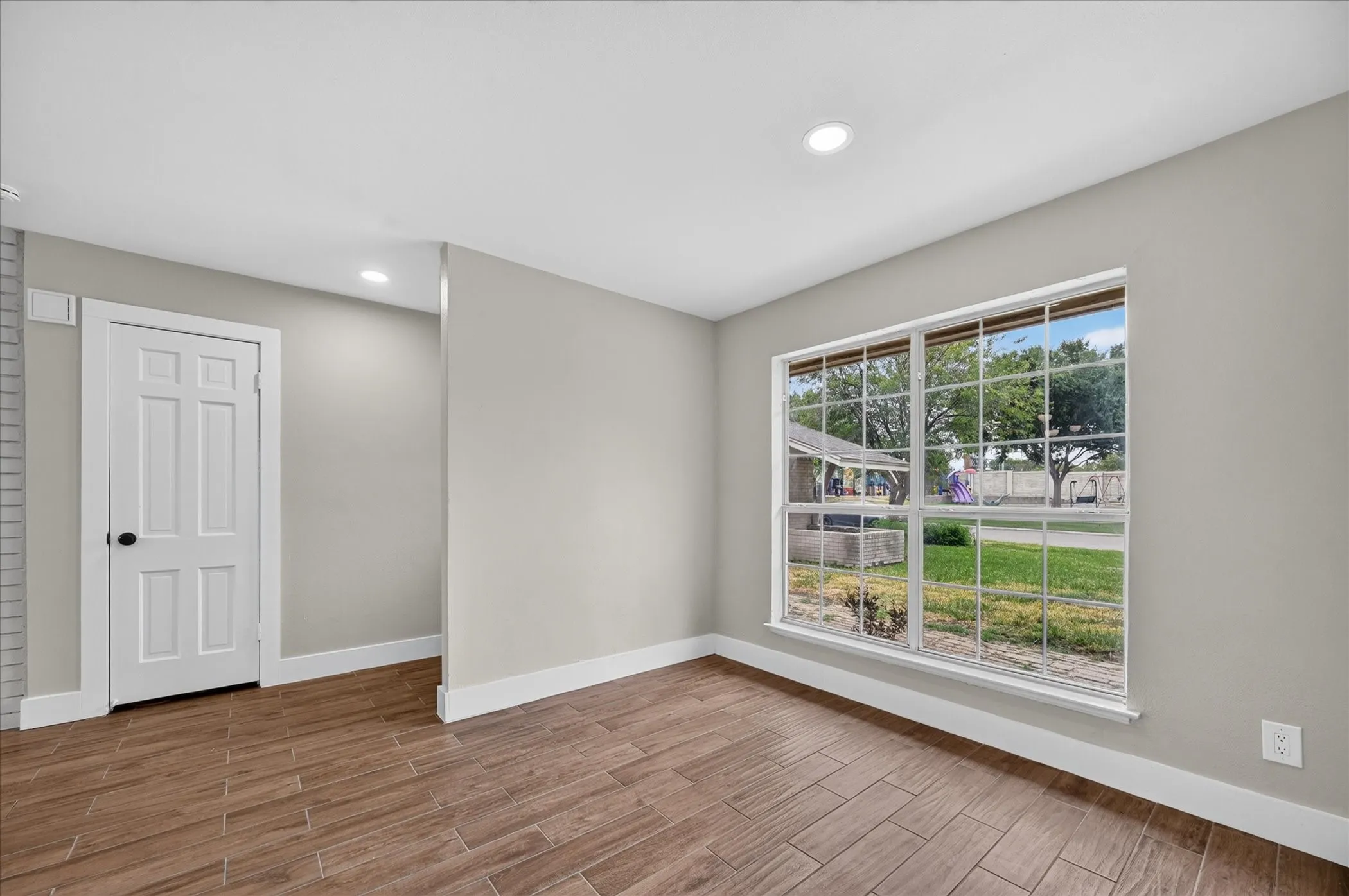 Wood-finish flooring, recessed lighting, neutral wall paint, white trim, and a multi-pane window