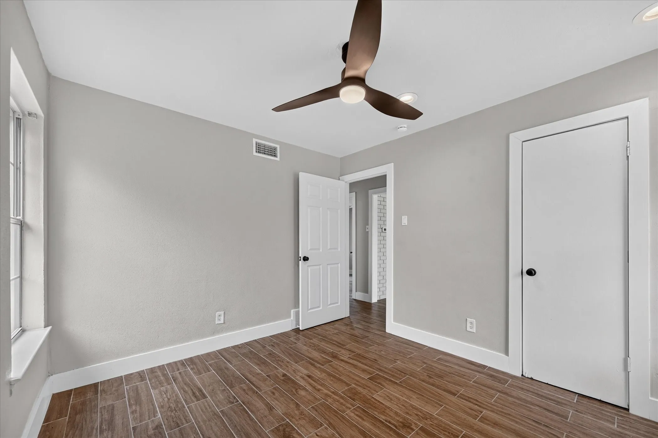 Wood-finish flooring, light gray walls, white trim, and a ceiling fan with integrated lighting