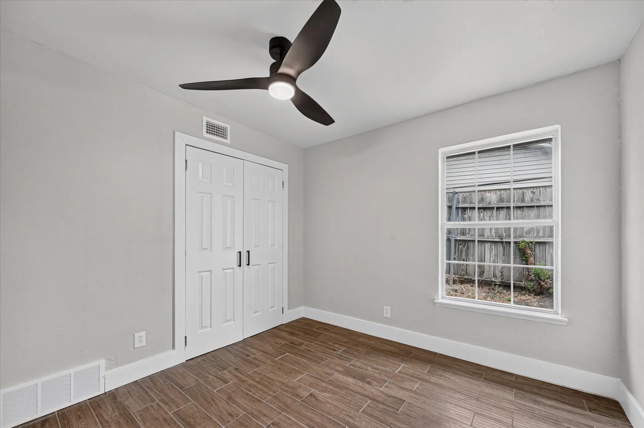 Wood-finish flooring, white bi-fold doors, modern ceiling fan with integrated lighting, and a white-framed window