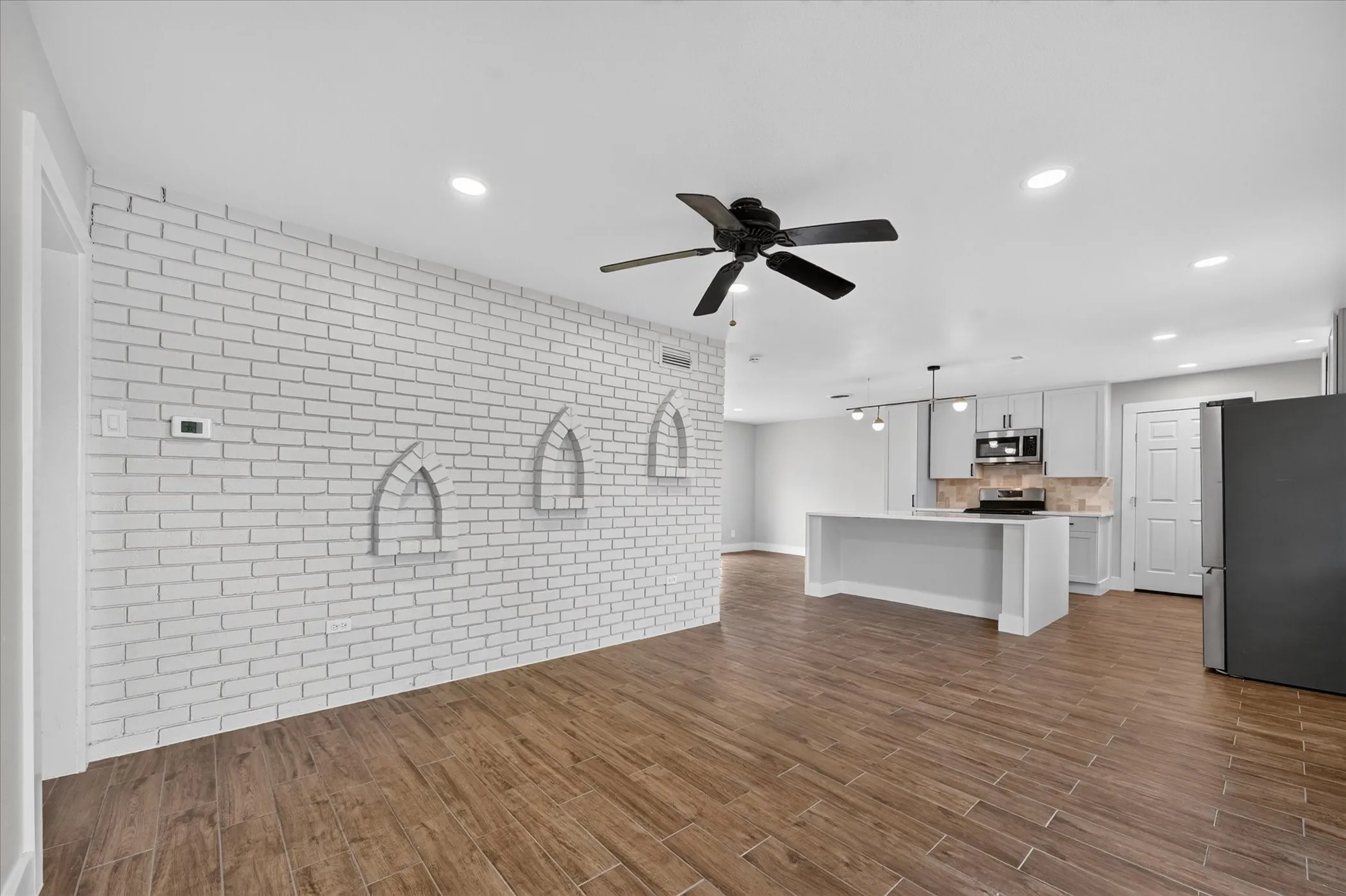 Exposed brick accent wall with arched niches, wood-finish flooring, recessed lighting, ceiling fan, and kitchen island with pendant lighting