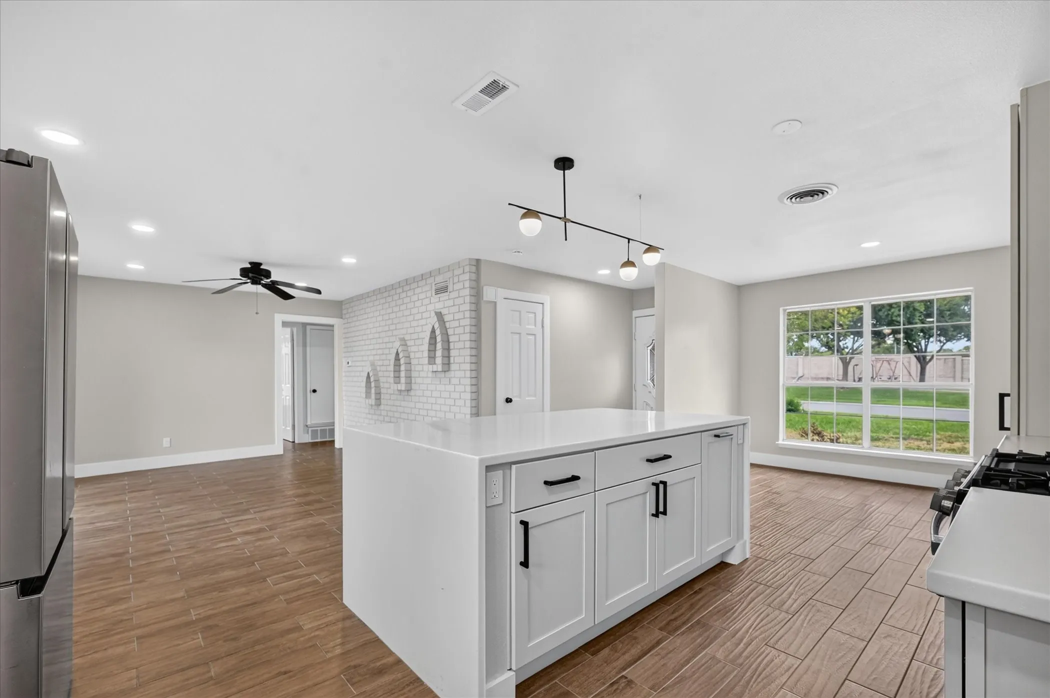 Kitchen island with white cabinetry and dark hardware, wood-finish flooring, recessed lighting, and a decorative exposed brick wall