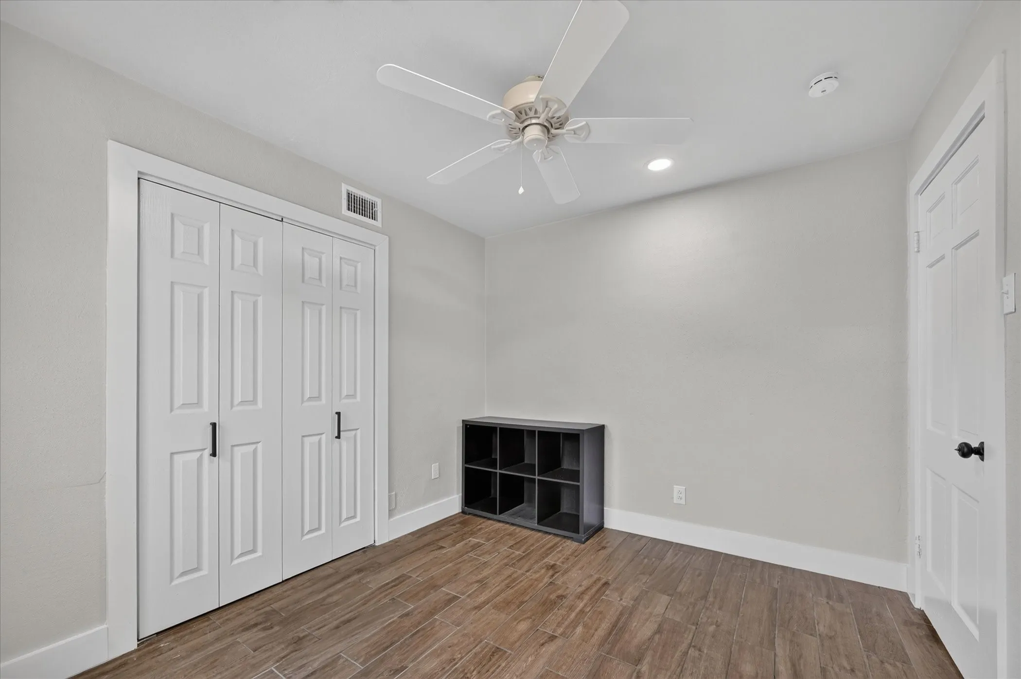 Wood-finish flooring, ceiling fan, recessed lighting, white paneled doors, and light neutral wall tones