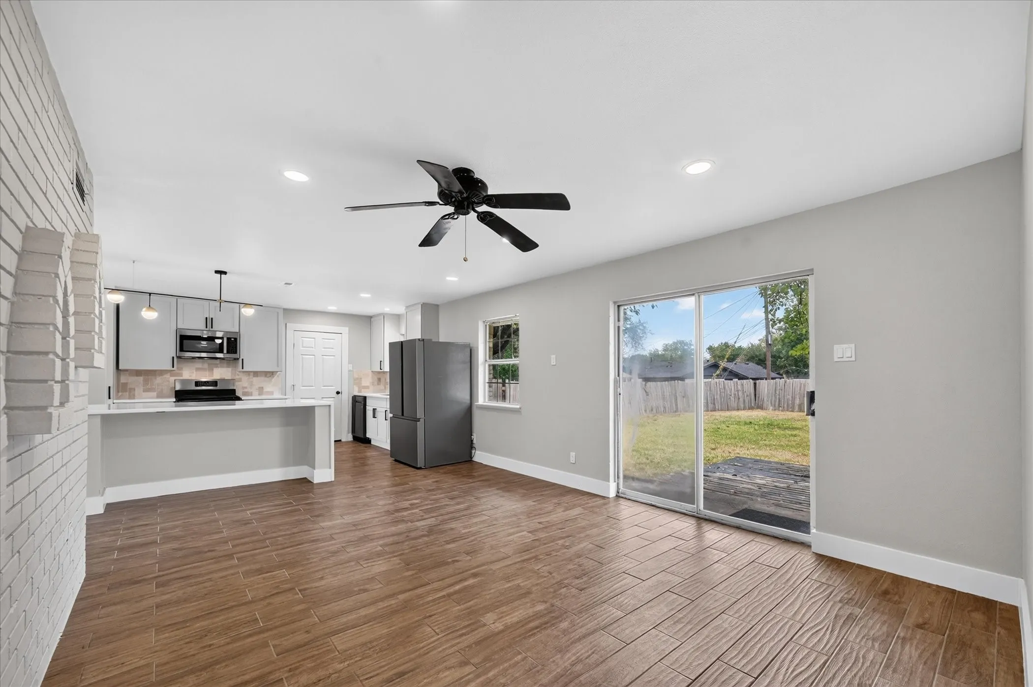 Wood-look tile flooring throughout, white brick accent wall, light gray cabinetry, stainless steel appliances, and sliding glass door access to the rear yard