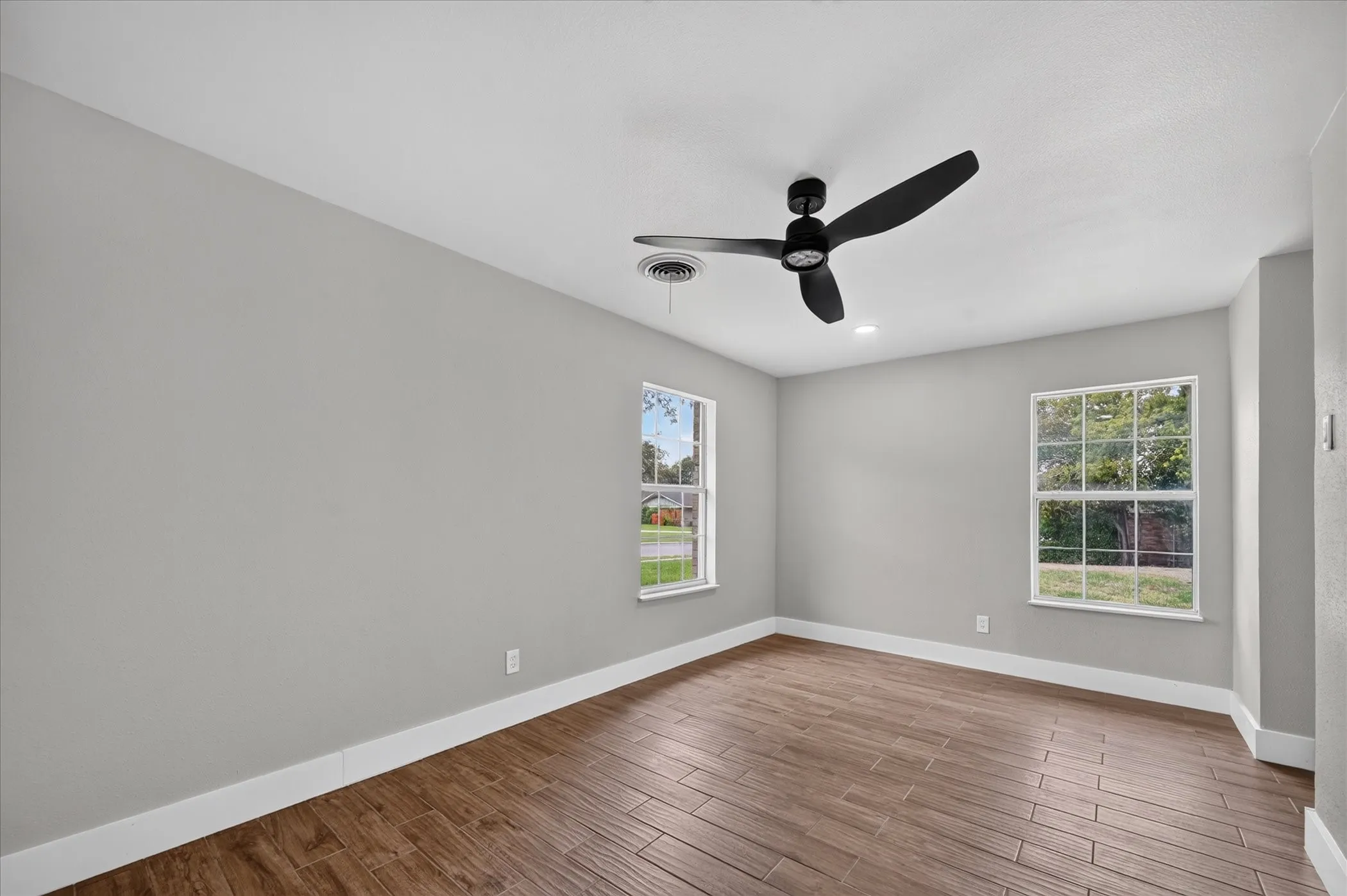 Wood-finish flooring, light gray wall tones, ceiling fan, and multiple windows with white frames