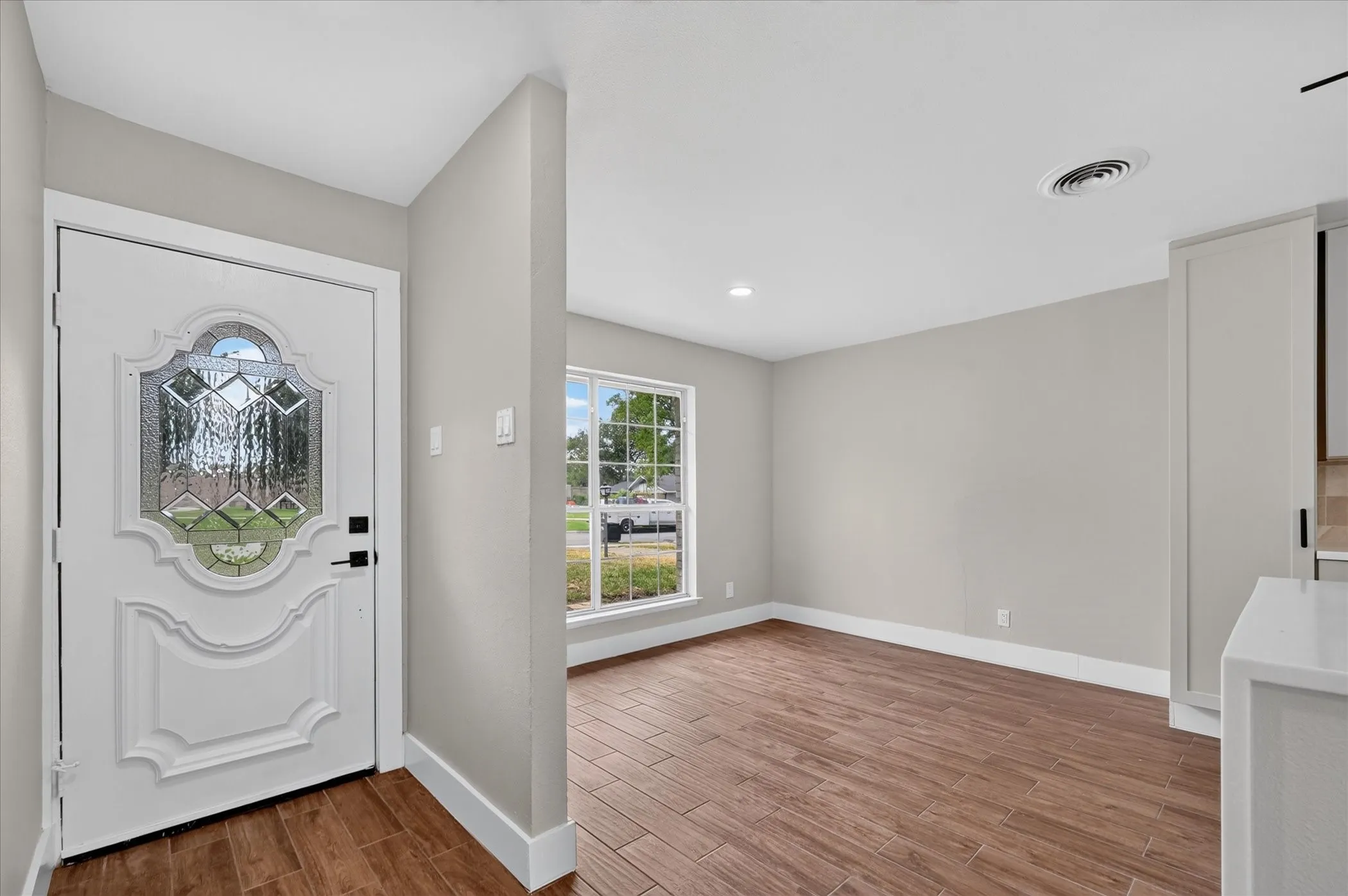 Decorative glass panel entry door, wood-look tile flooring, recessed lighting, and a front-facing window