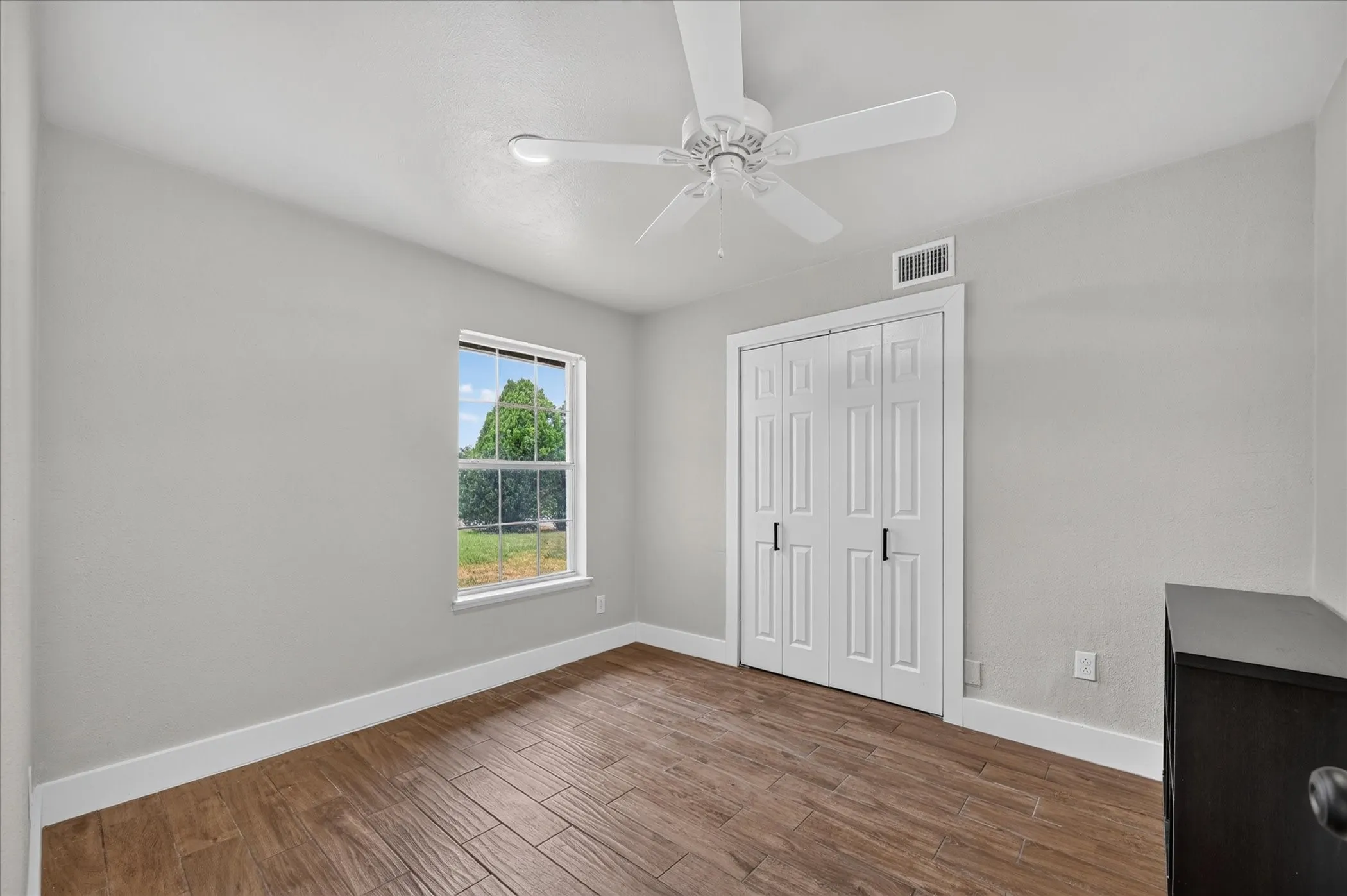Wood-finish flooring with white baseboards, a white ceiling fan, and a double-door closet