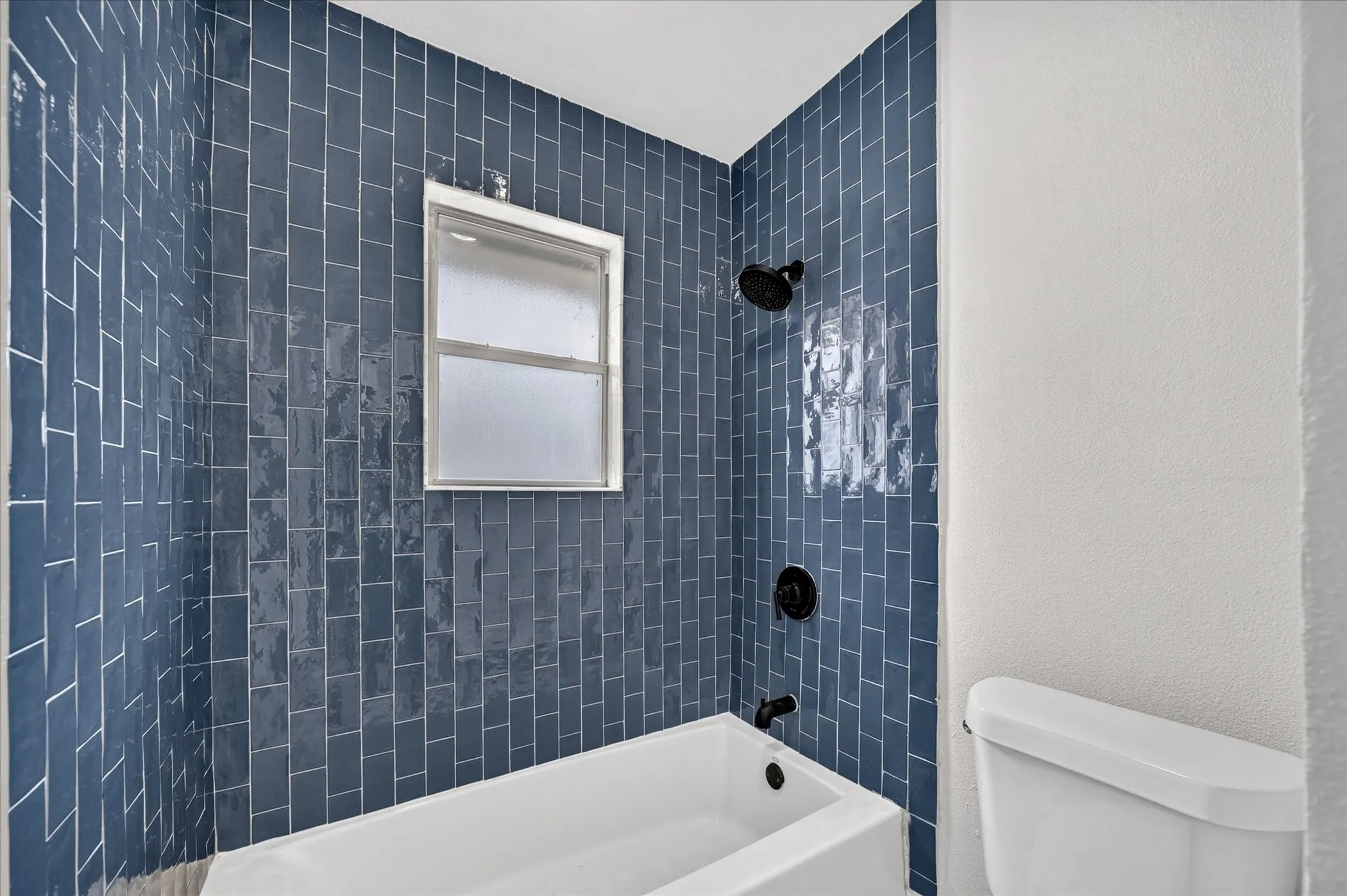 Shower/tub combination with deep blue subway tile surround, matte black shower fixtures, and an integrated window