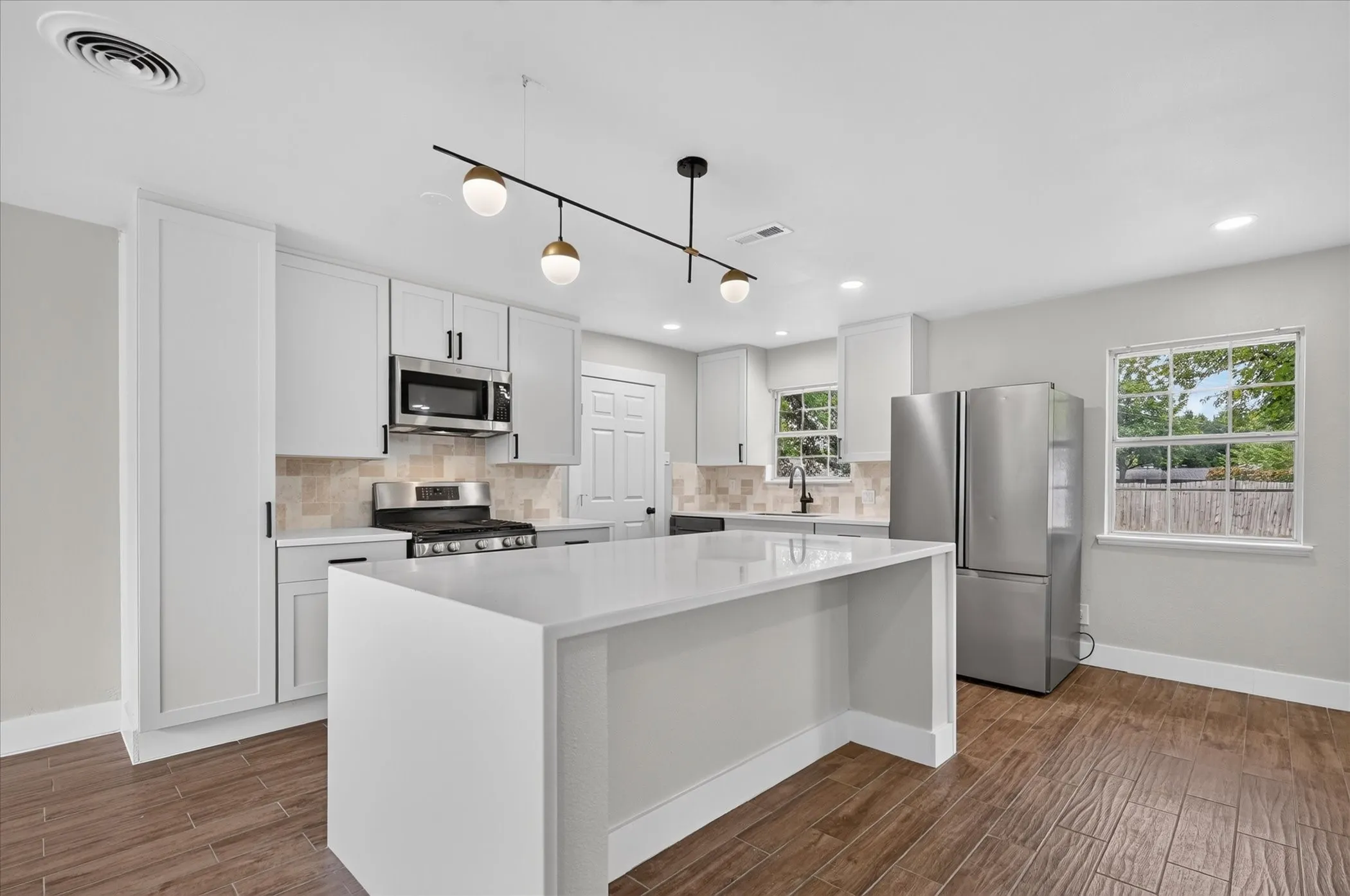 Kitchen featuring white cabinetry, stainless steel appliances, a center island with a white countertop, and wood-finish flooring